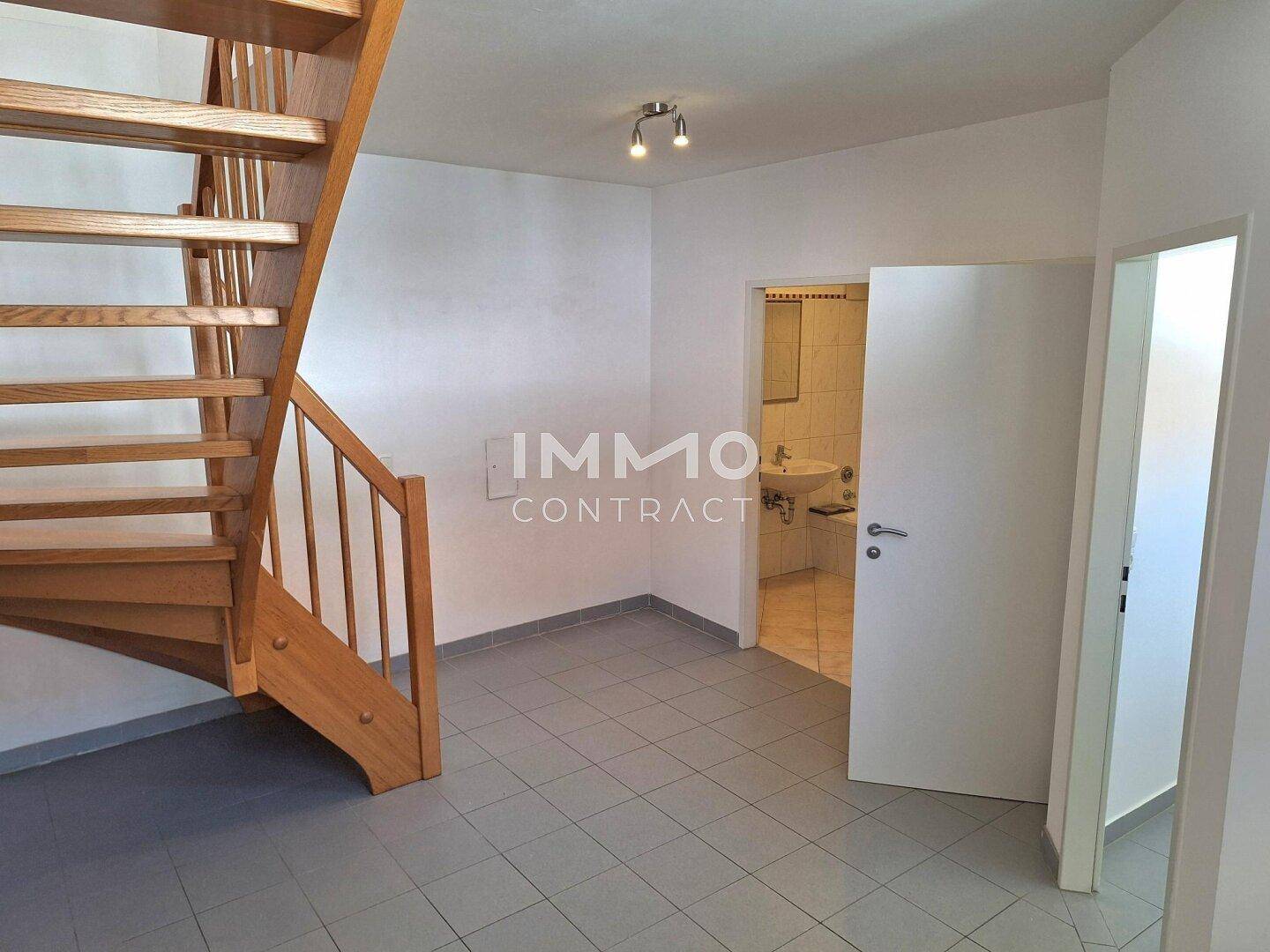 Flur mit Holztreppe und Zugang zu einem Badezimmer, gefliestem Boden.