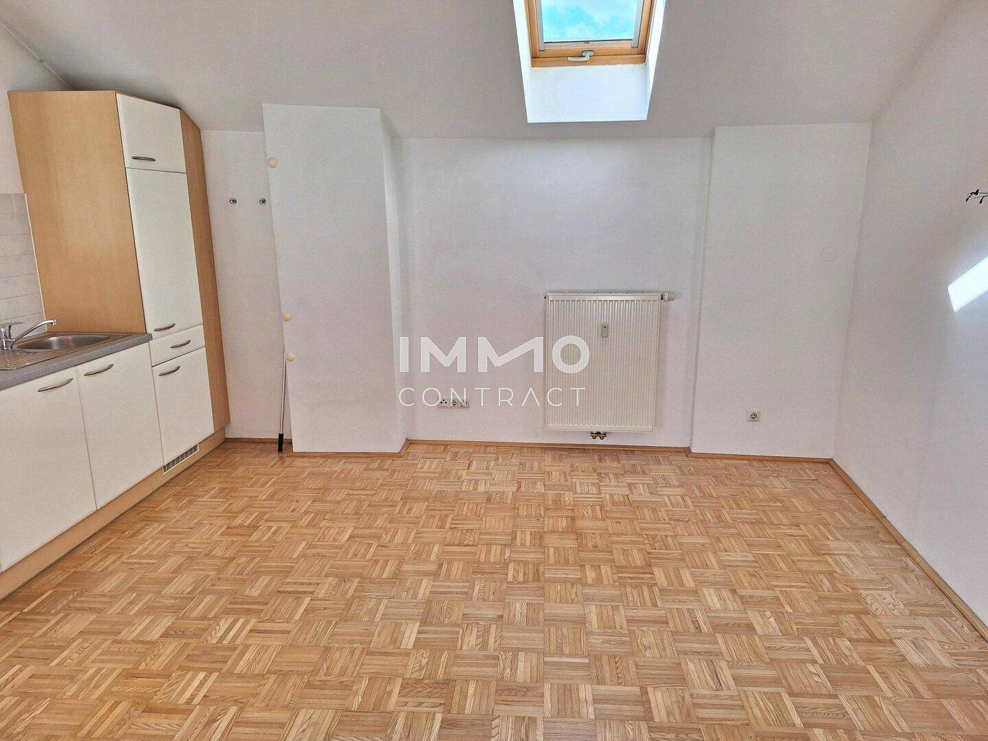 Leerer offener Raum mit Parkettboden, Dachfenster und integrierter Küchenzeile.