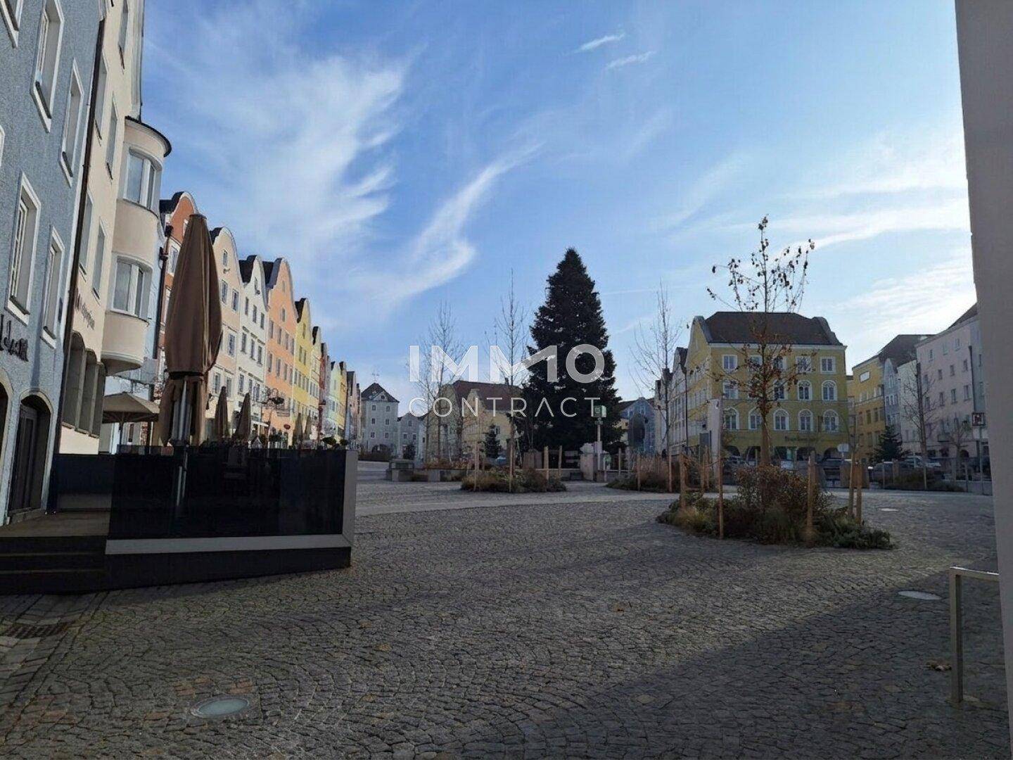 Weitläufiger, gepflasterter Stadtplatz mit Bäumen und umliegenden historischen Gebäuden.
