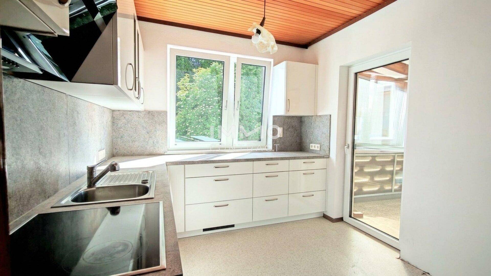Funktionale Küche mit weißen Schränken, Induktionskochfeld und Fenster mit Blick ins Grüne.