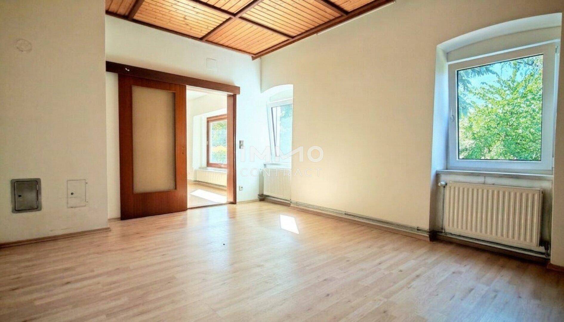 Helles Zimmer mit Holzboden, Holzdecke und einer praktischen Schiebetür zu einem angrenzenden Raum.