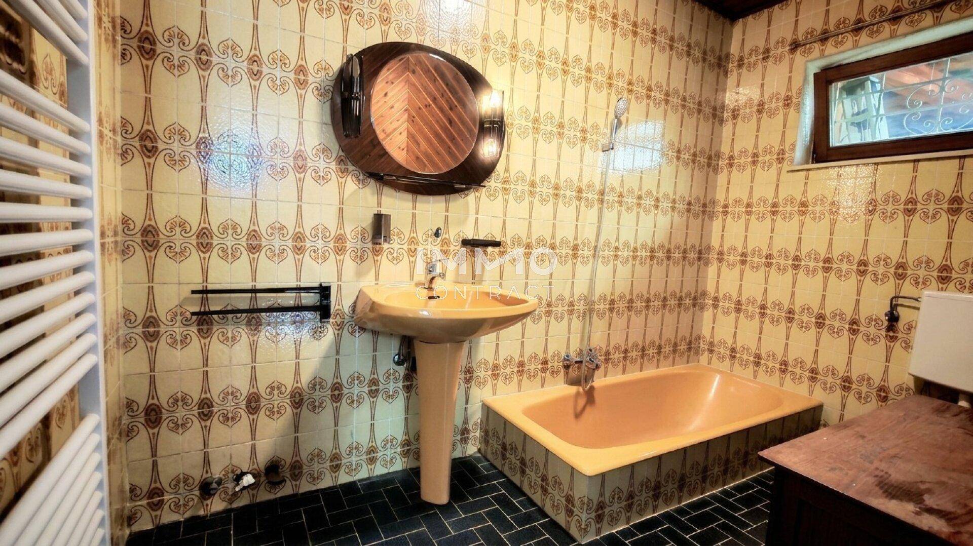 Badezimmer im Stil der 80er Jahre mit gemusterten Fliesen, gelber Badewanne und Waschbecken.