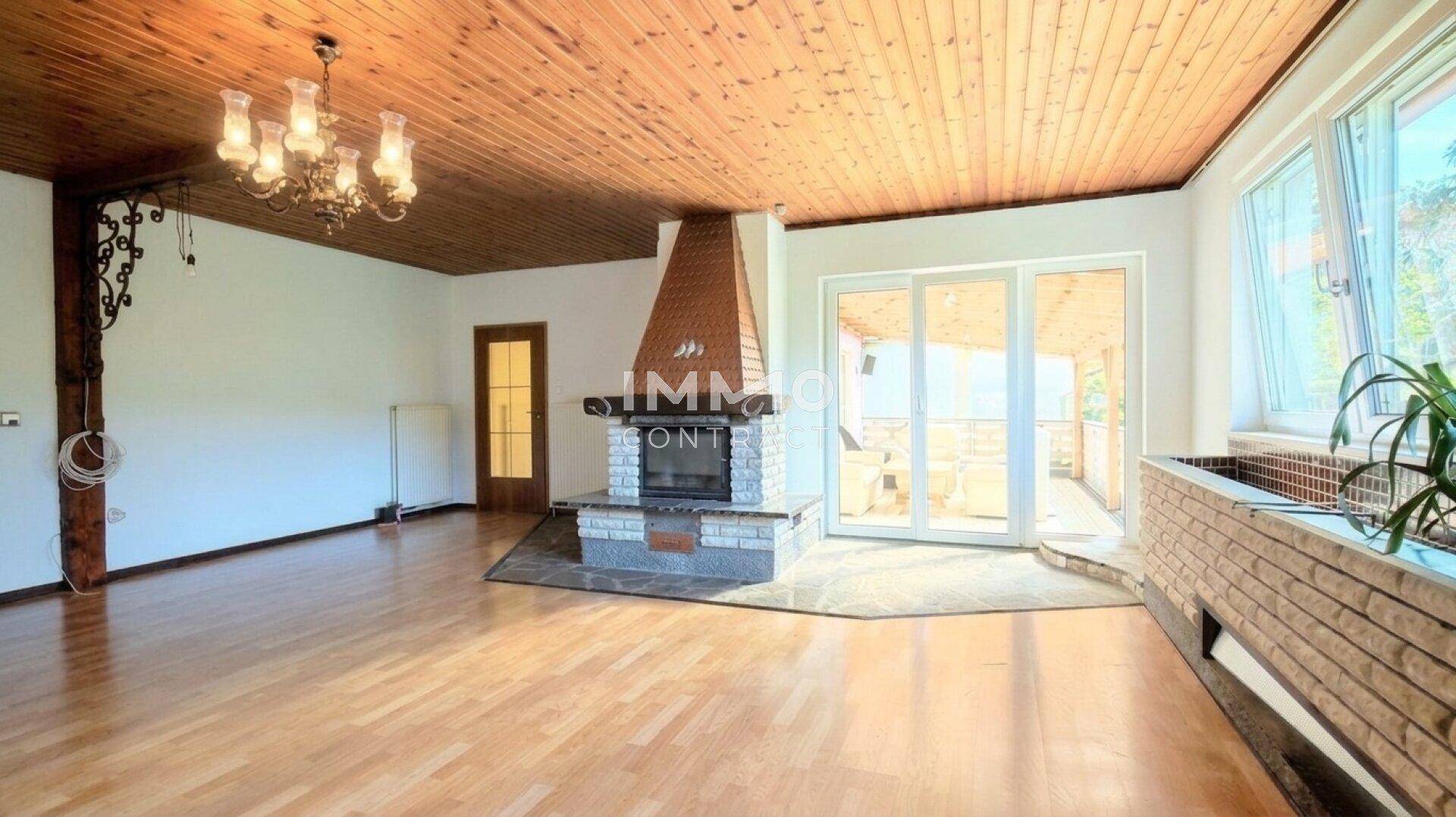 Gemütliches Wohnzimmer mit traditionellem Kamin, Holzbalkendecke und Zugang zu einem Außenbereich.