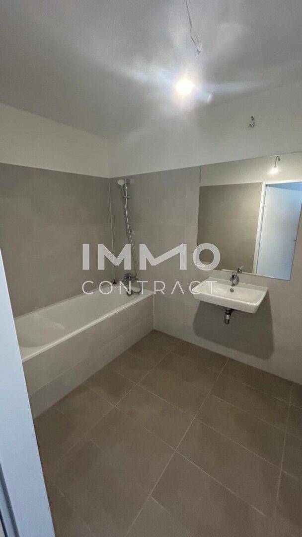 Modernes Badezimmer mit Badewanne, Einzelwaschbecken und großem Spiegel, gefliest in Grau.