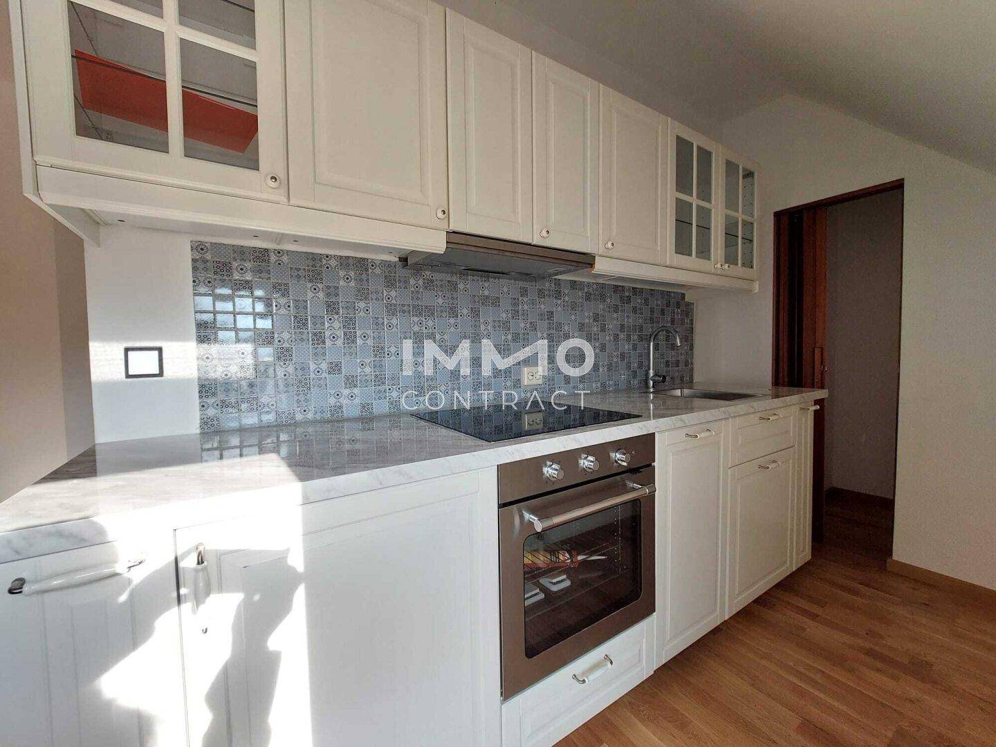 Moderne Küche mit weißen Schränken, heller Arbeitsplatte und gemusterter Fliesenrückwand.