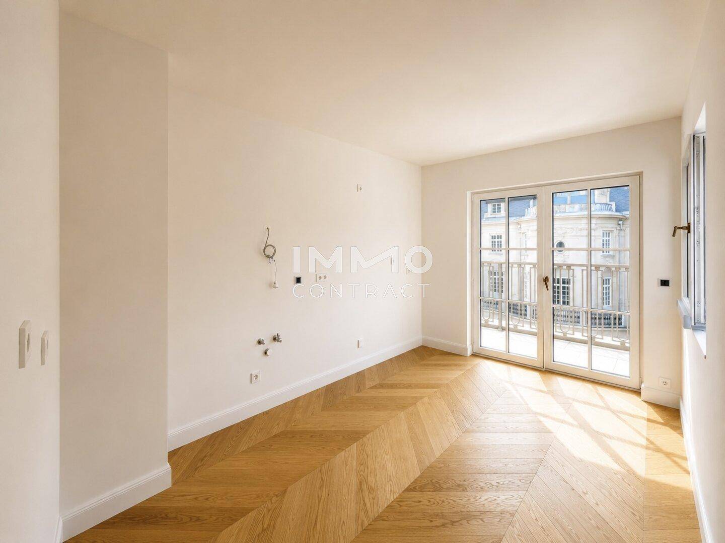 Heller Raum mit Fischgrätparkett und Zugang zu einem französischen Balkon.