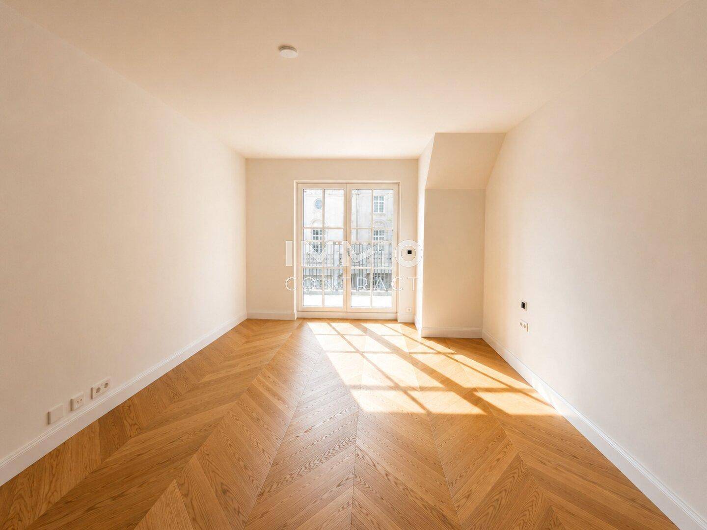 Heller Raum mit Fischgrätparkett und Sonnenlicht, das durch den französischen Balkon fällt.