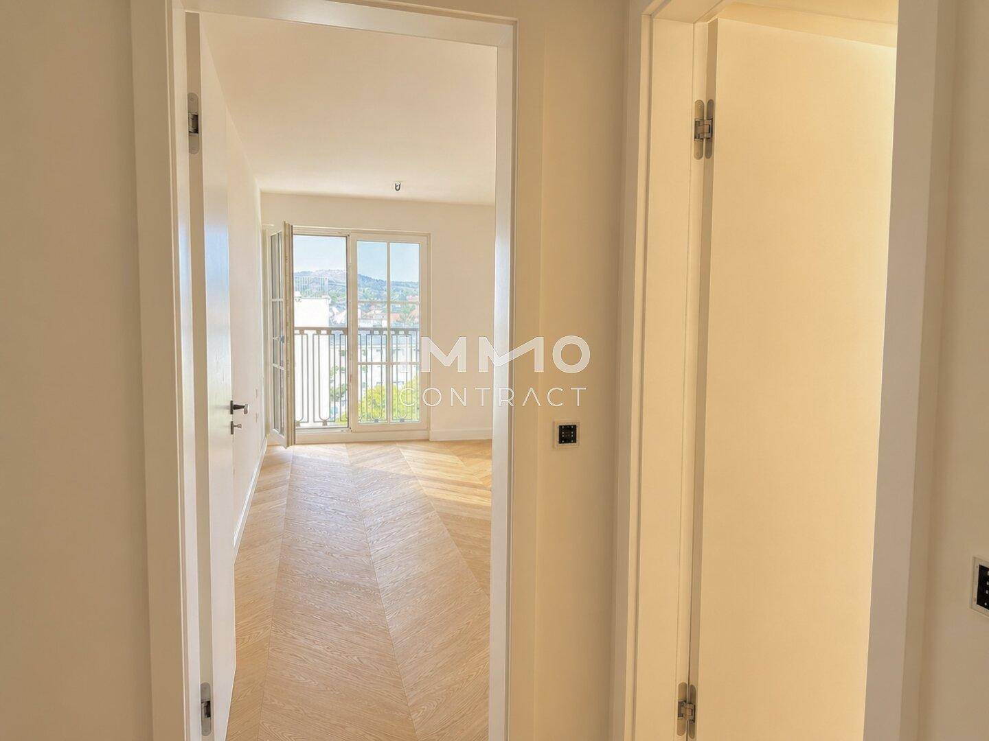 Heller Flur mit Blick in ein angrenzendes Zimmer mit Fischgrätparkett und Balkonzugang.