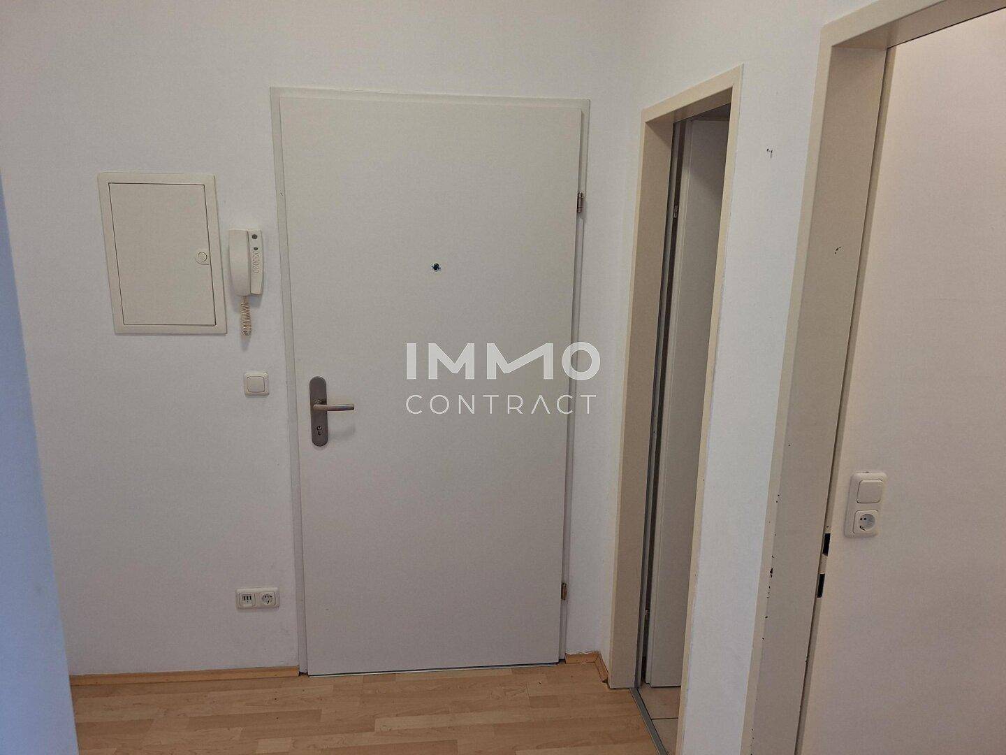Eingangsbereich mit weißer Tür, Gegensprechanlage und hellem Holzboden.