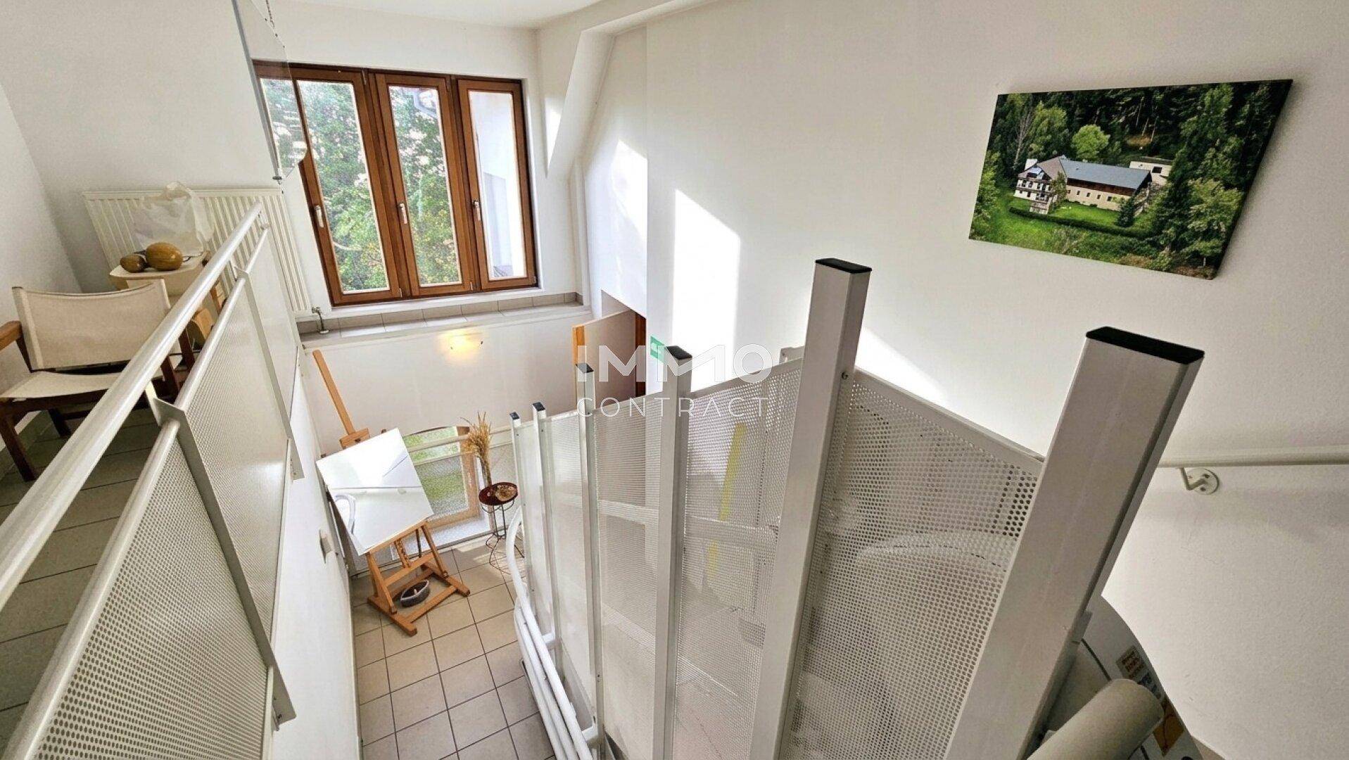 Heller Treppenaufgang mit großen Fenstern und Blick auf die grüne Umgebung.