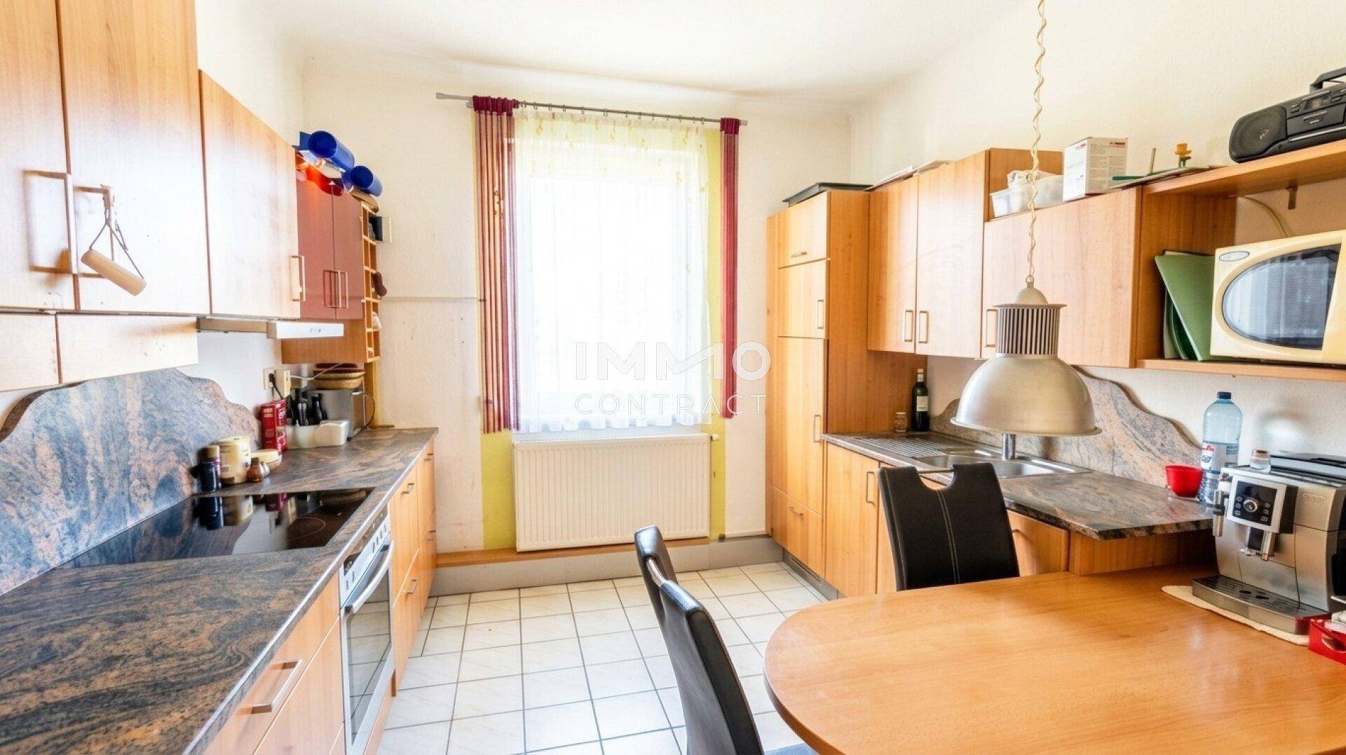 Funktionale Küche mit Holzschränken, Granitarbeitsplatten und einem Essbereich am Fenster.
