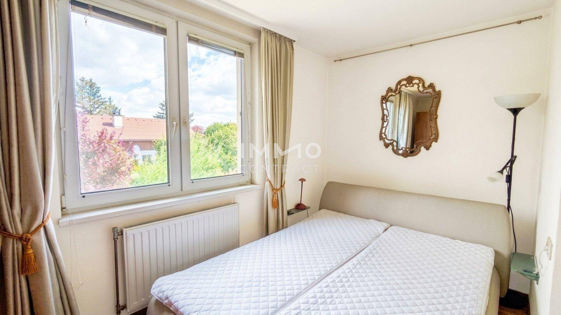 Helles Schlafzimmer mit Doppelbett, großem Fenster und Blick ins Grüne.