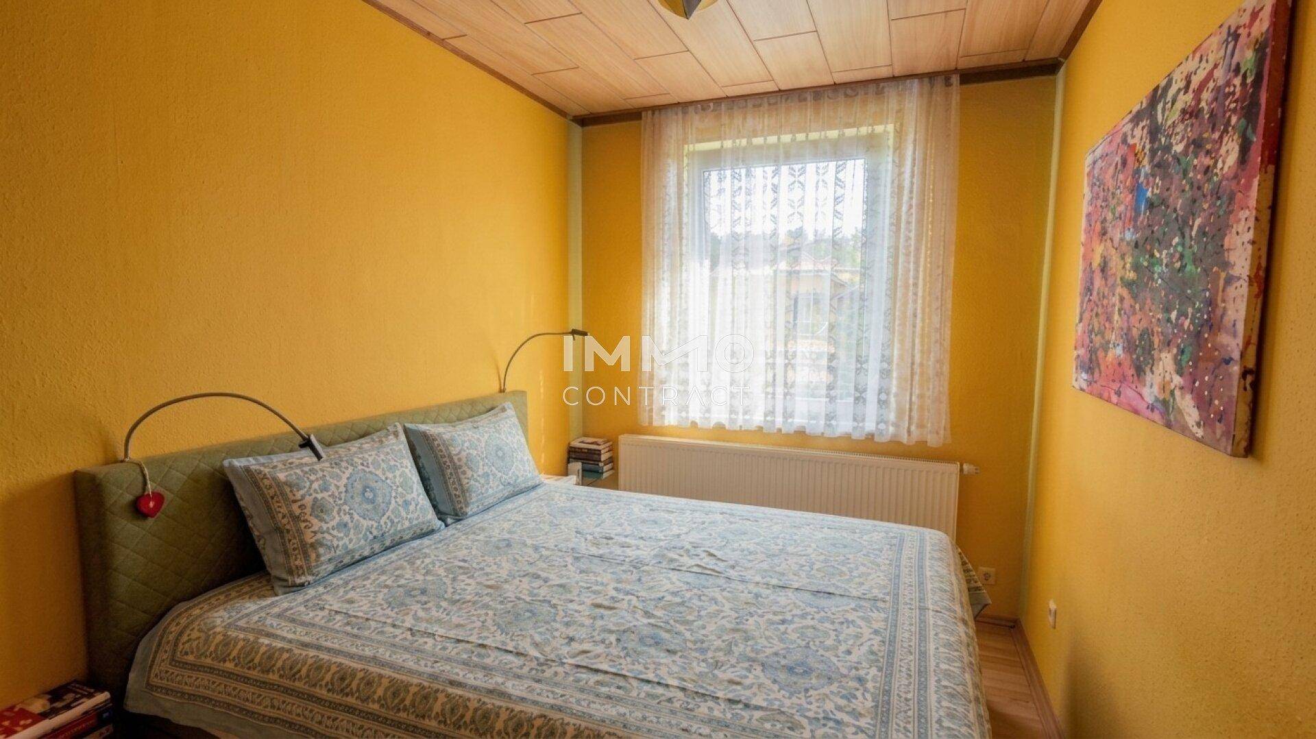 Gemütliches Schlafzimmer mit gelben Wänden, Doppelbett und einem Fenster mit Vorhängen.