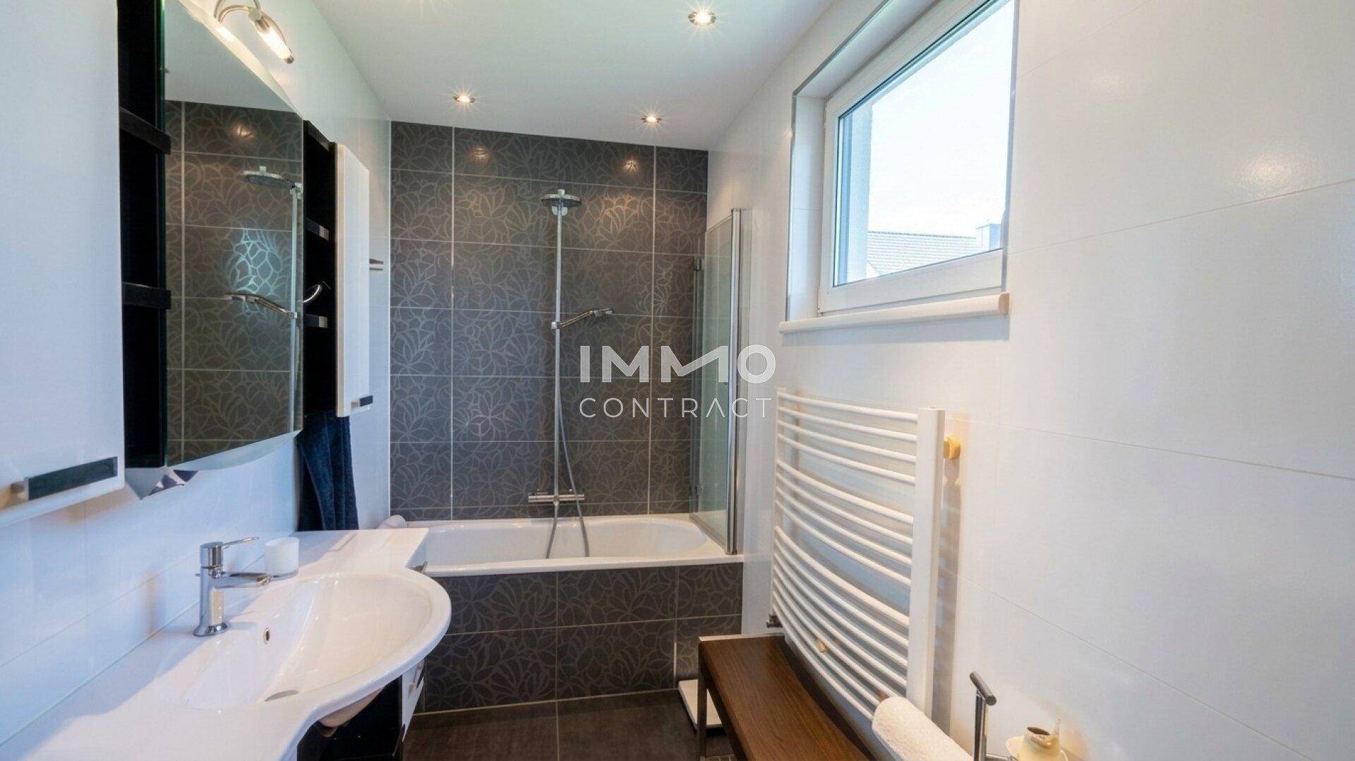 Modernes Badezimmer mit Badewanne, Dusche, dunklen Fliesen und einem Fenster für Tageslicht.