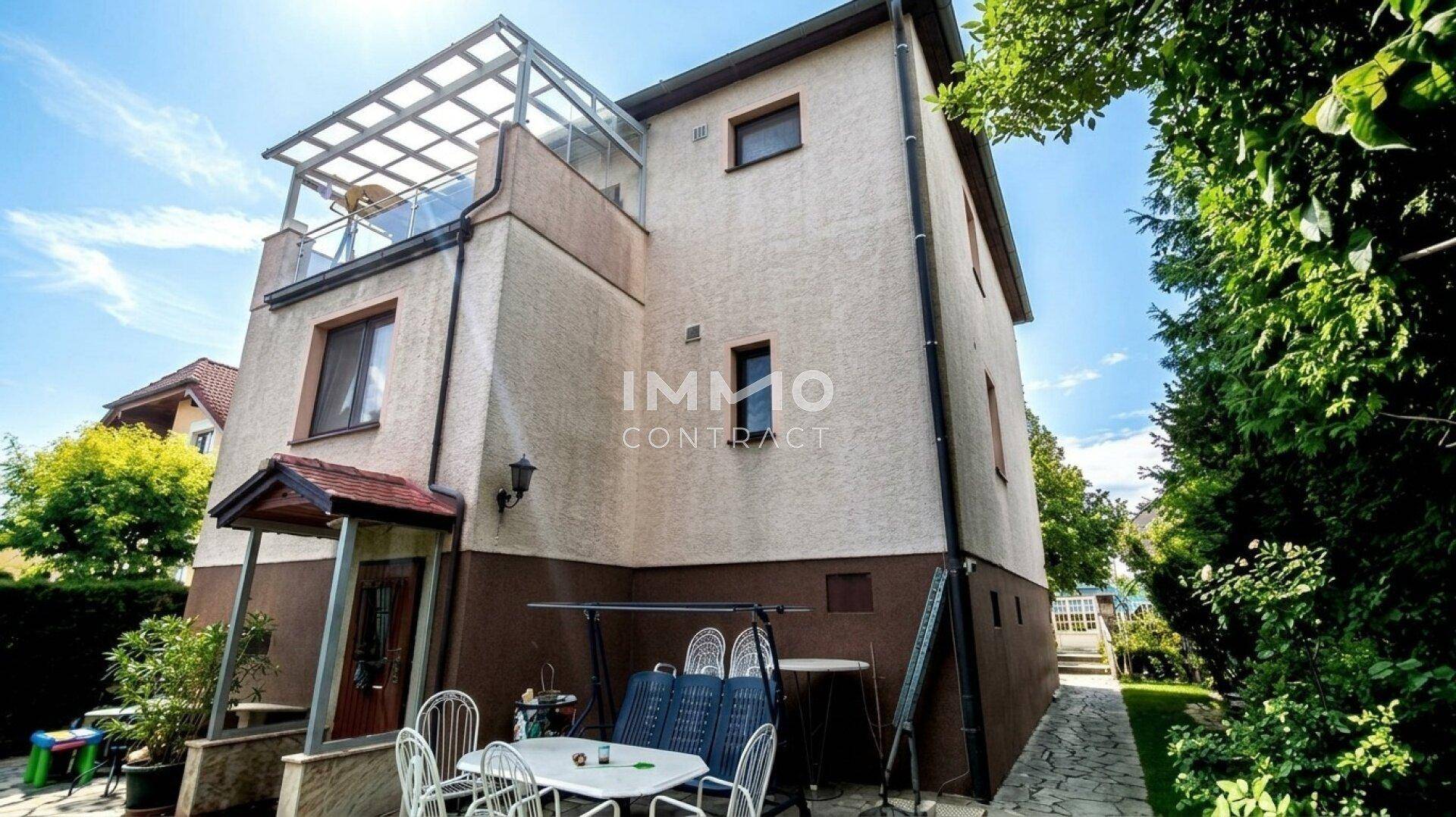Rückansicht des Hauses mit überdachtem Eingangsbereich und einer kleinen Terrasse mit Sitzgelegenheiten.