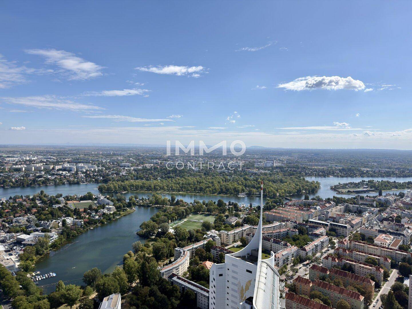 Weitläufiger Blick aus der Höhe auf die Stadt, Seen und grüne Inseln unter blauem Himmel.