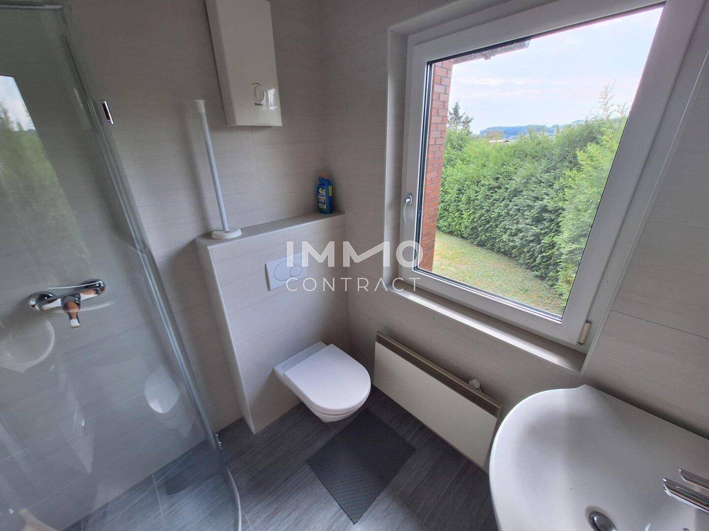 Modernes Badezimmer mit Dusche, wandhängendem WC und Fenster mit Blick ins Grüne.