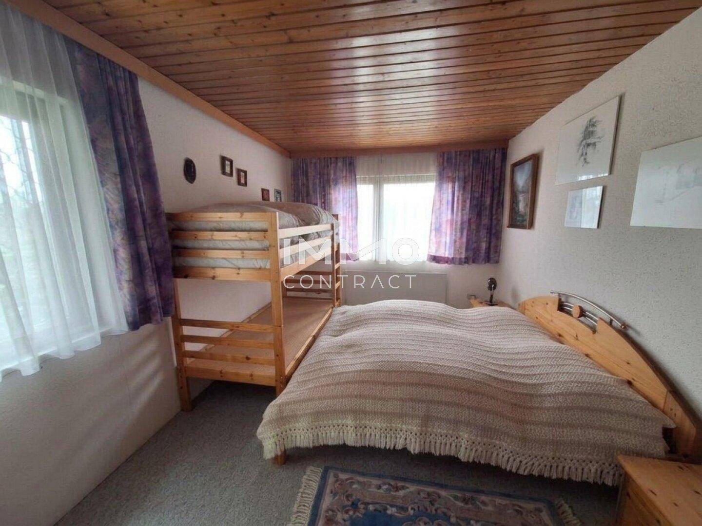 Schlafzimmer mit Doppelbett und Etagenbett, Holzbalkendecke und Teppichboden.