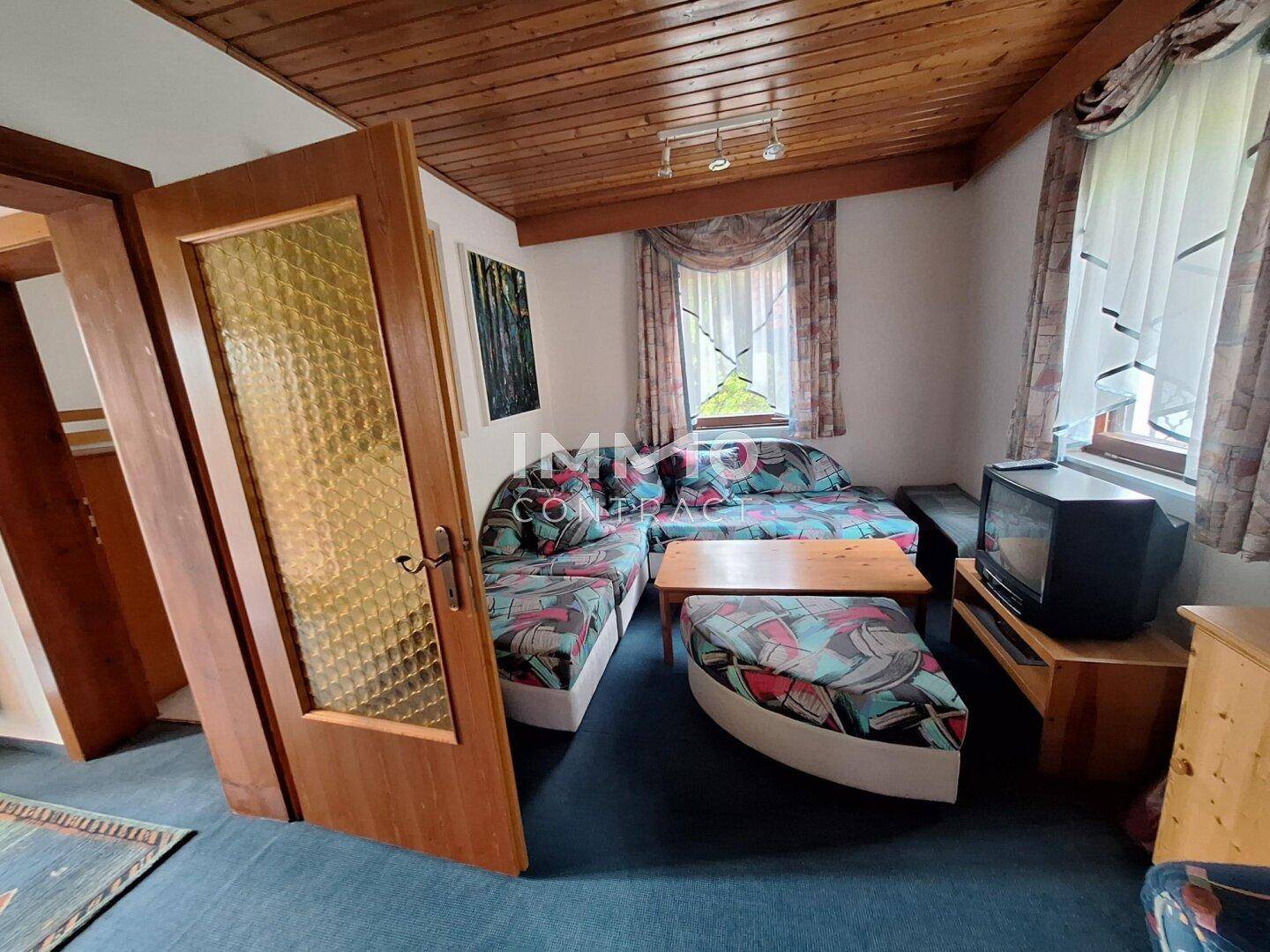 Gemütliches Wohnzimmer im Landhausstil mit Holzbalkendecke und farbenfrohen Sofas.