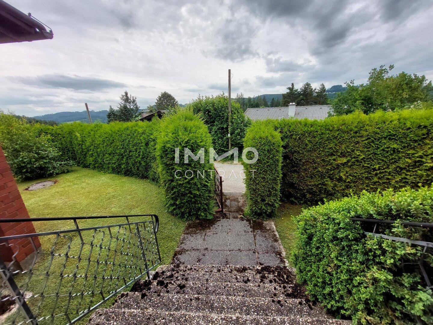 Steintreppe führt durch einen gepflegten Garten mit hohen Hecken und Blick auf die Landschaft.