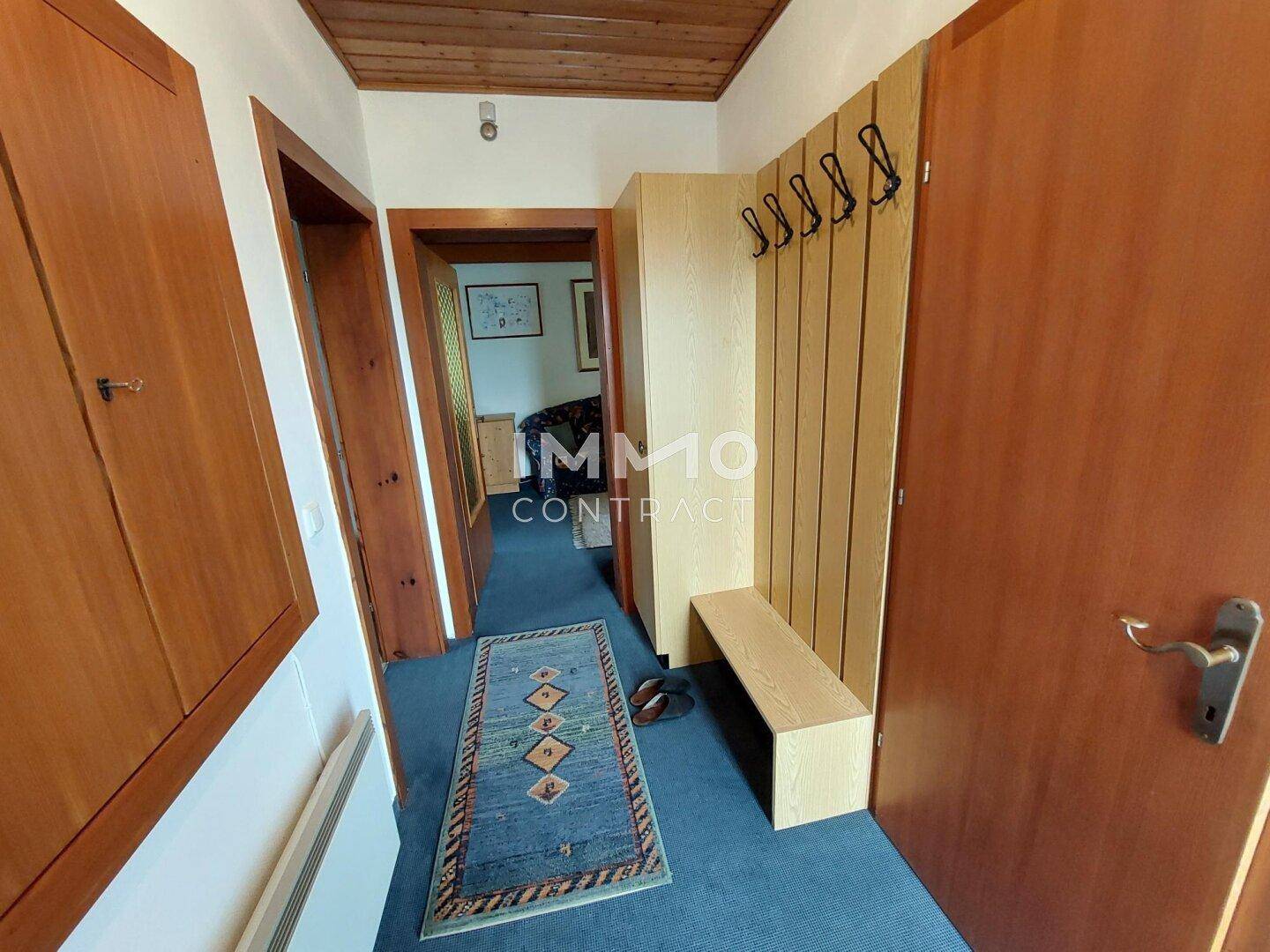 Eingangsbereich mit Garderobe, Holzdecke und Teppichboden, führt zu weiteren Räumen.