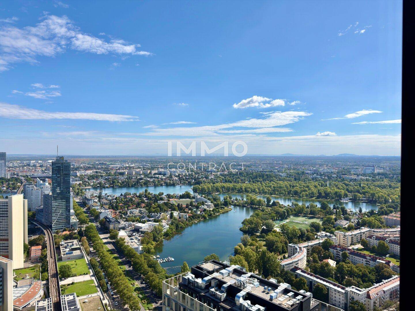 Weitläufige Luftaufnahme einer Stadtlandschaft mit Fluss, Seen und vielen Grünflächen unter blauem Himmel.