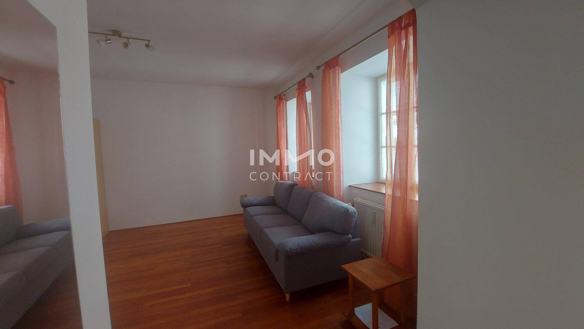 Gemütliches Wohnzimmer mit Sofa, Holzboden und großen Fenstern.