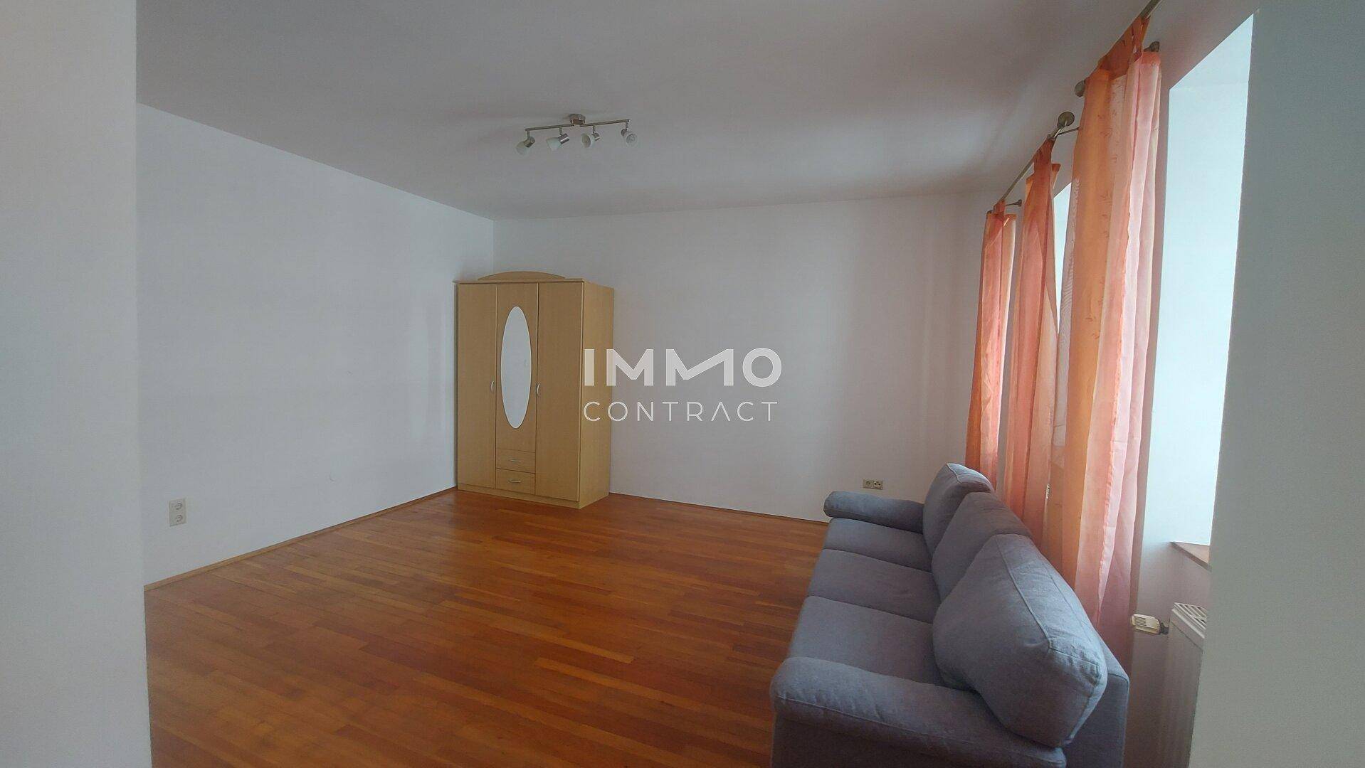 Helles Wohnzimmer mit Sofa, Kleiderschrank und Holzboden.