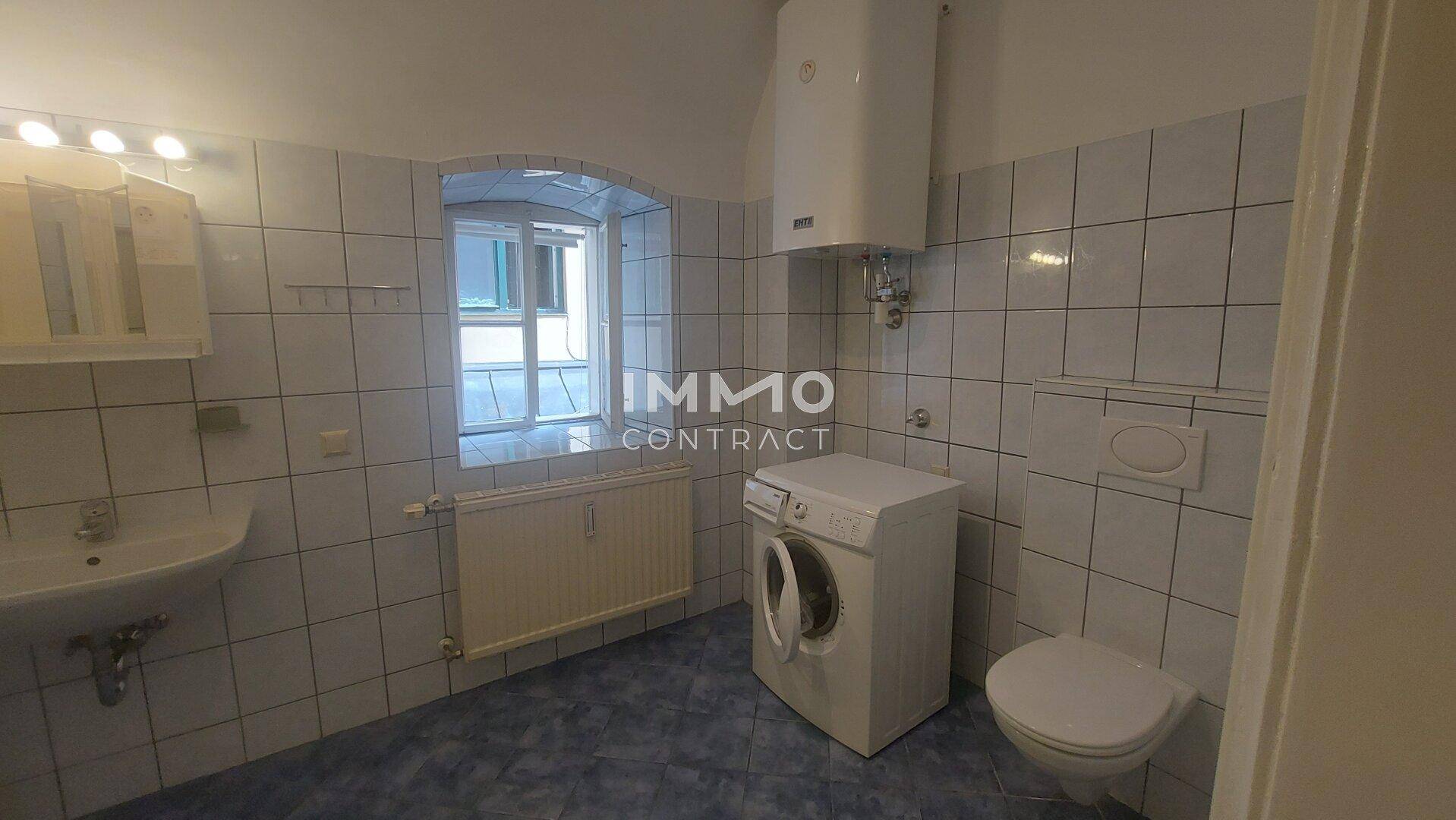 Gefliestes Badezimmer mit WC, Waschbecken, Waschmaschine und Fenster.