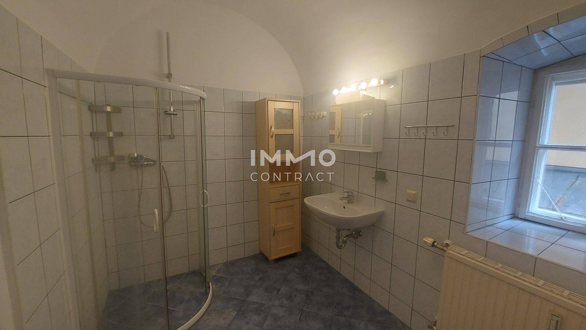 Badezimmer mit Duschkabine, Waschbecken, Spiegelschrank und Fenster.