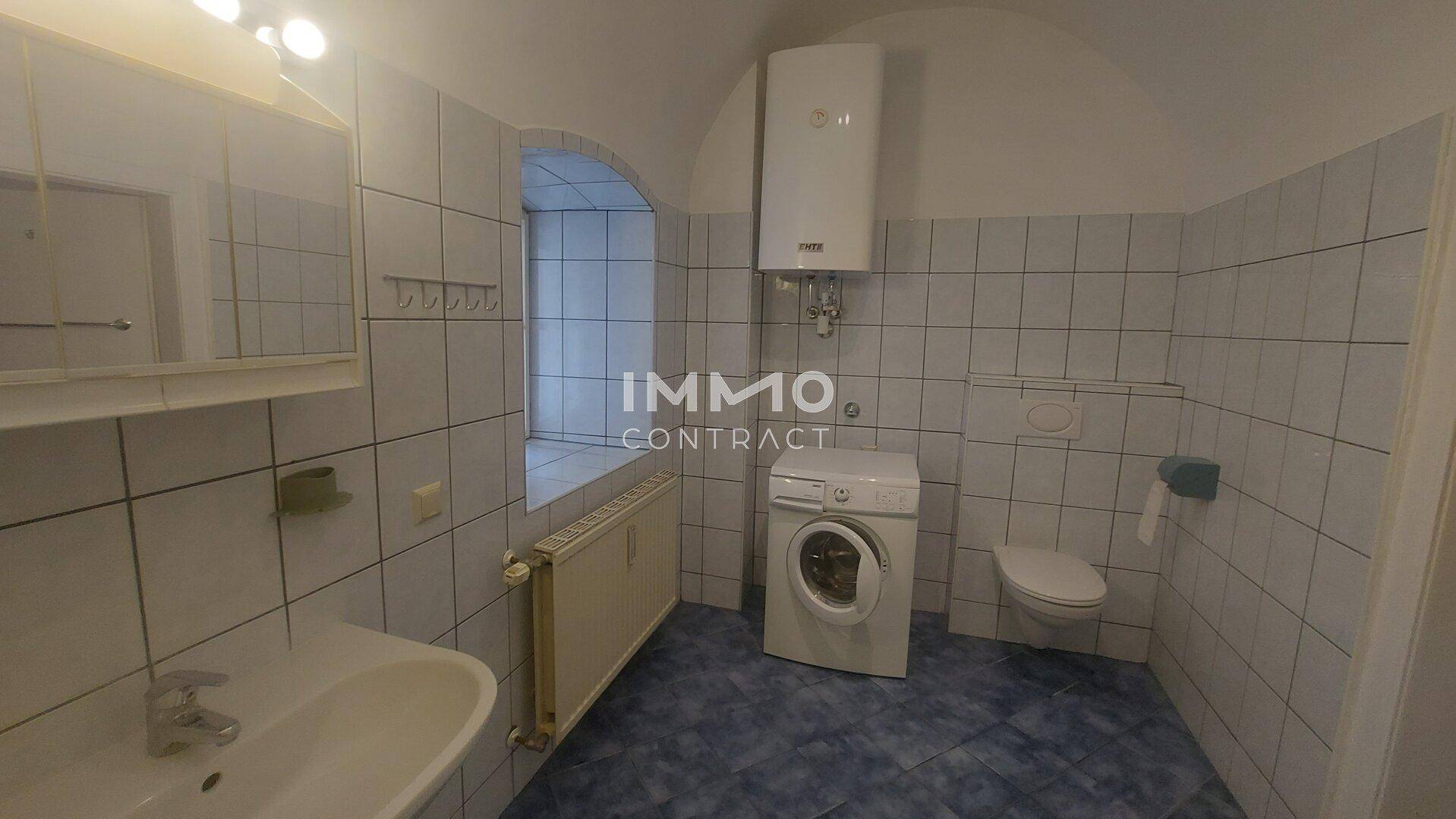 Gefliestes Badezimmer mit WC, Waschbecken, Waschmaschine und Fenster.