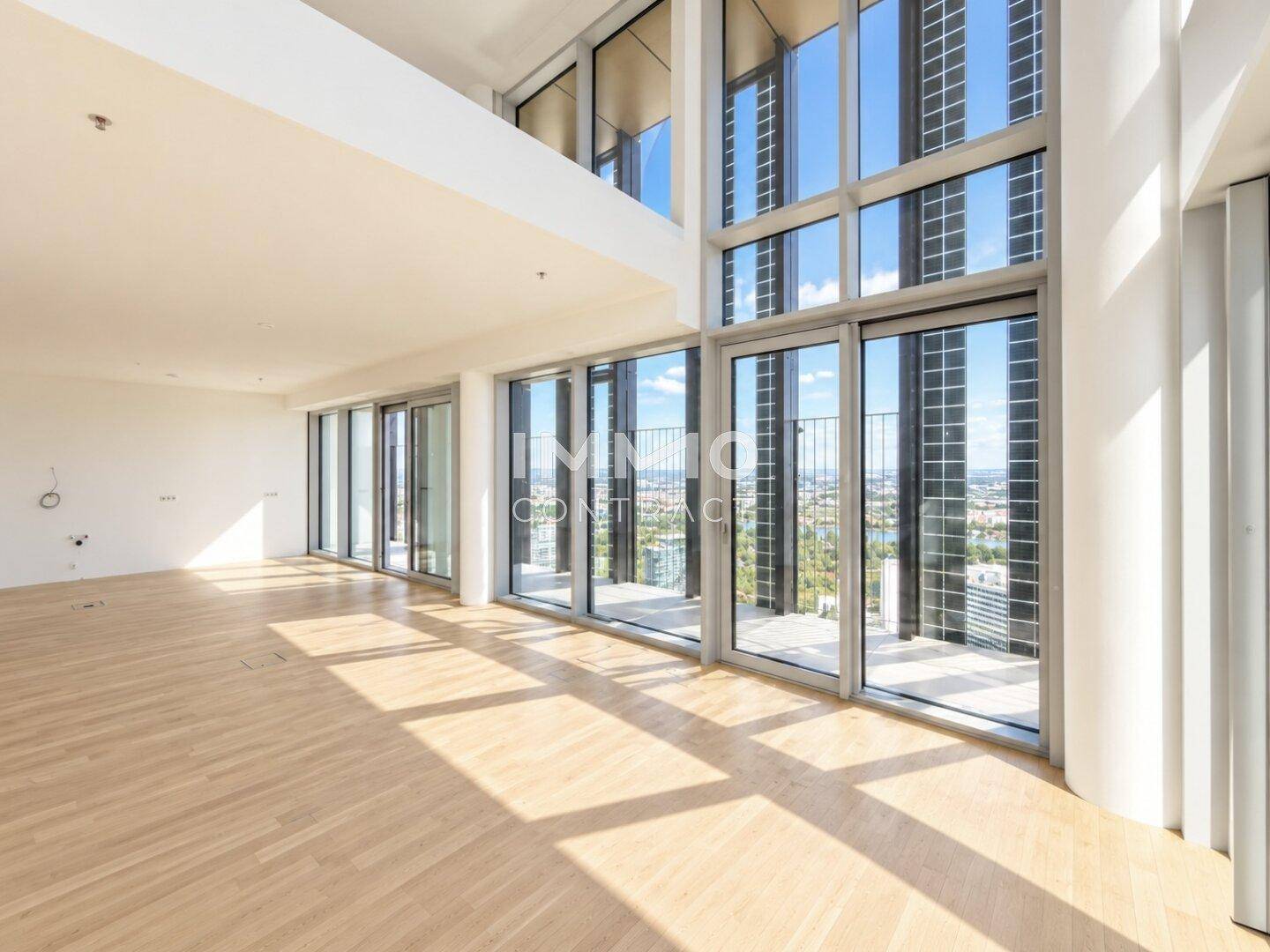 Großzügiger, leerer Wohnbereich mit hohen Decken, Holzboden und Zugang zu einem Balkon.