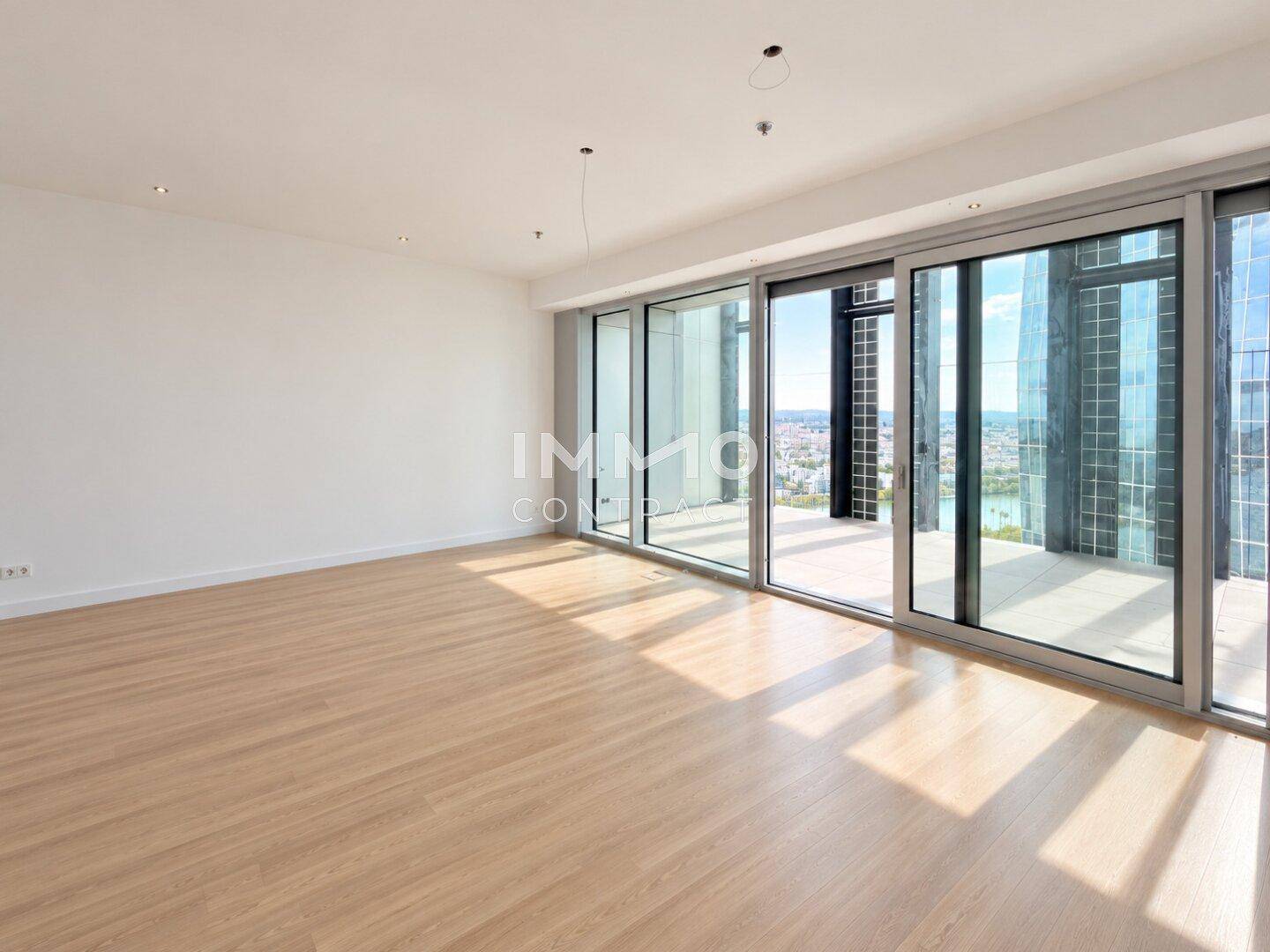 Heller, leerer Wohnraum mit Holzfußboden und großen Schiebetüren mit Blick auf die Stadt und das Wasser.