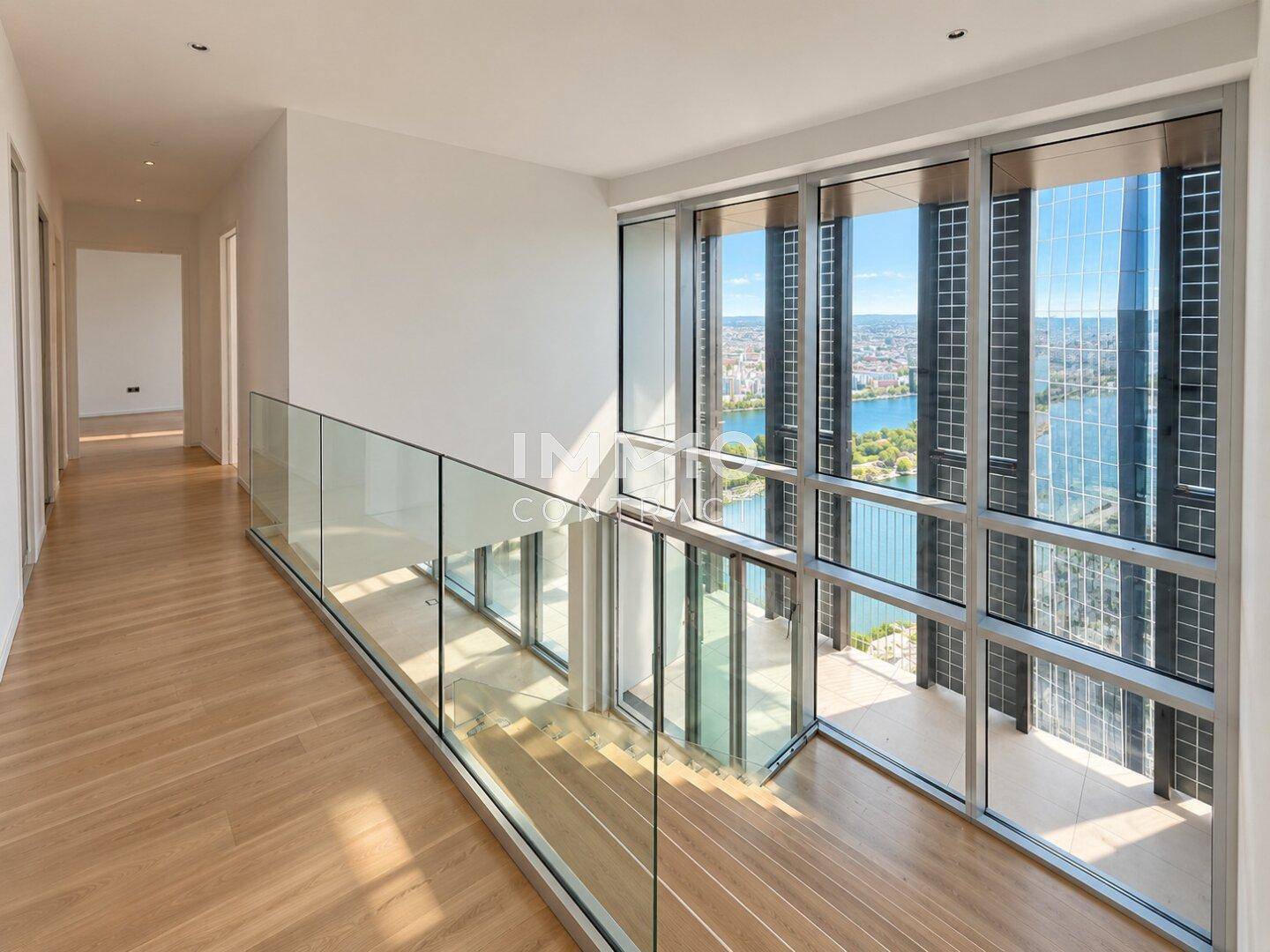 Heller Flur mit Holzfußboden, Glasgeländer und Panoramafenstern mit Blick auf die Stadt und das Wasser.