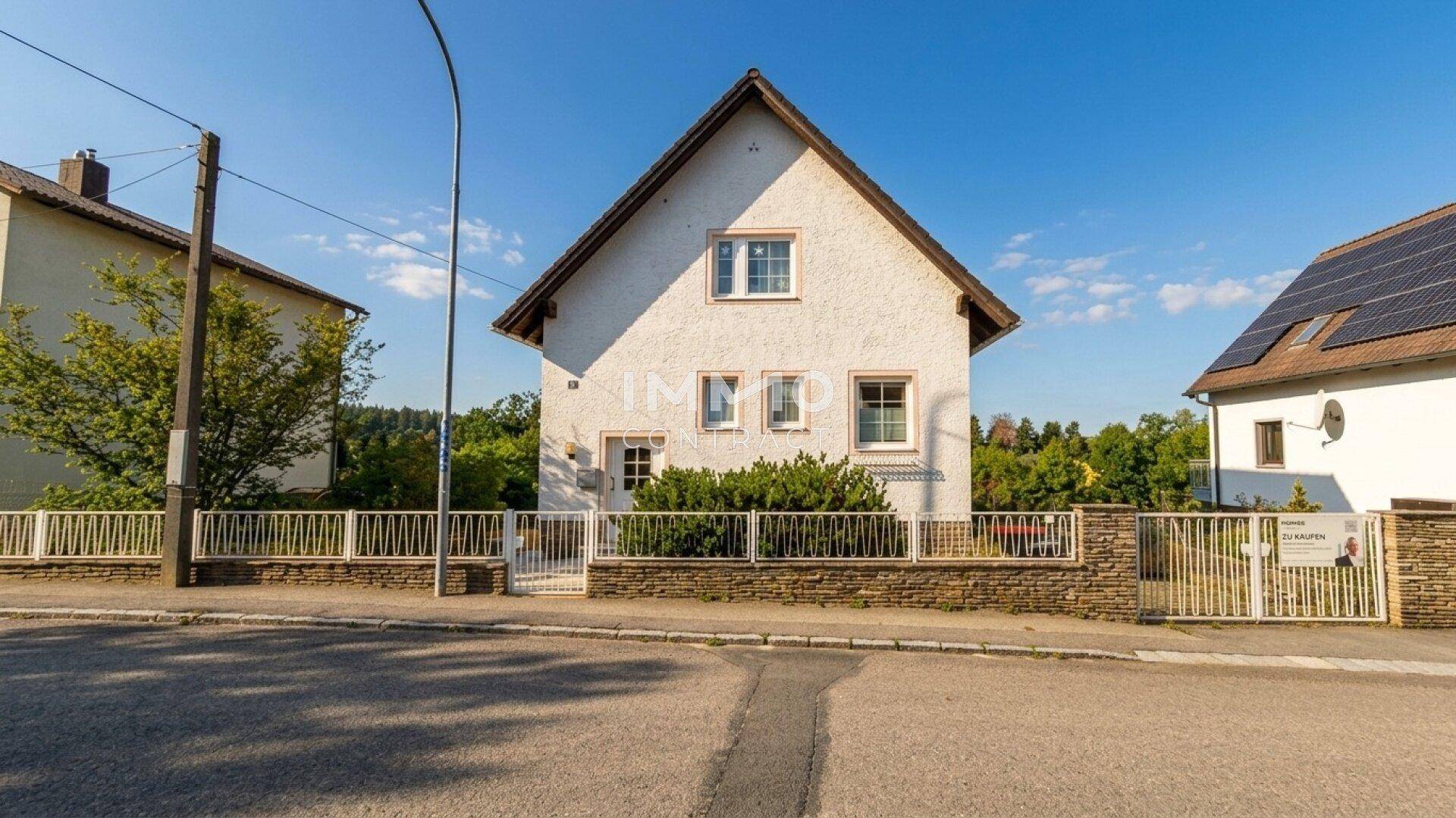 Weitwinkelansicht des weißen Einfamilienhauses mit Vorgarten und Solaranlage auf dem Nachbardach.