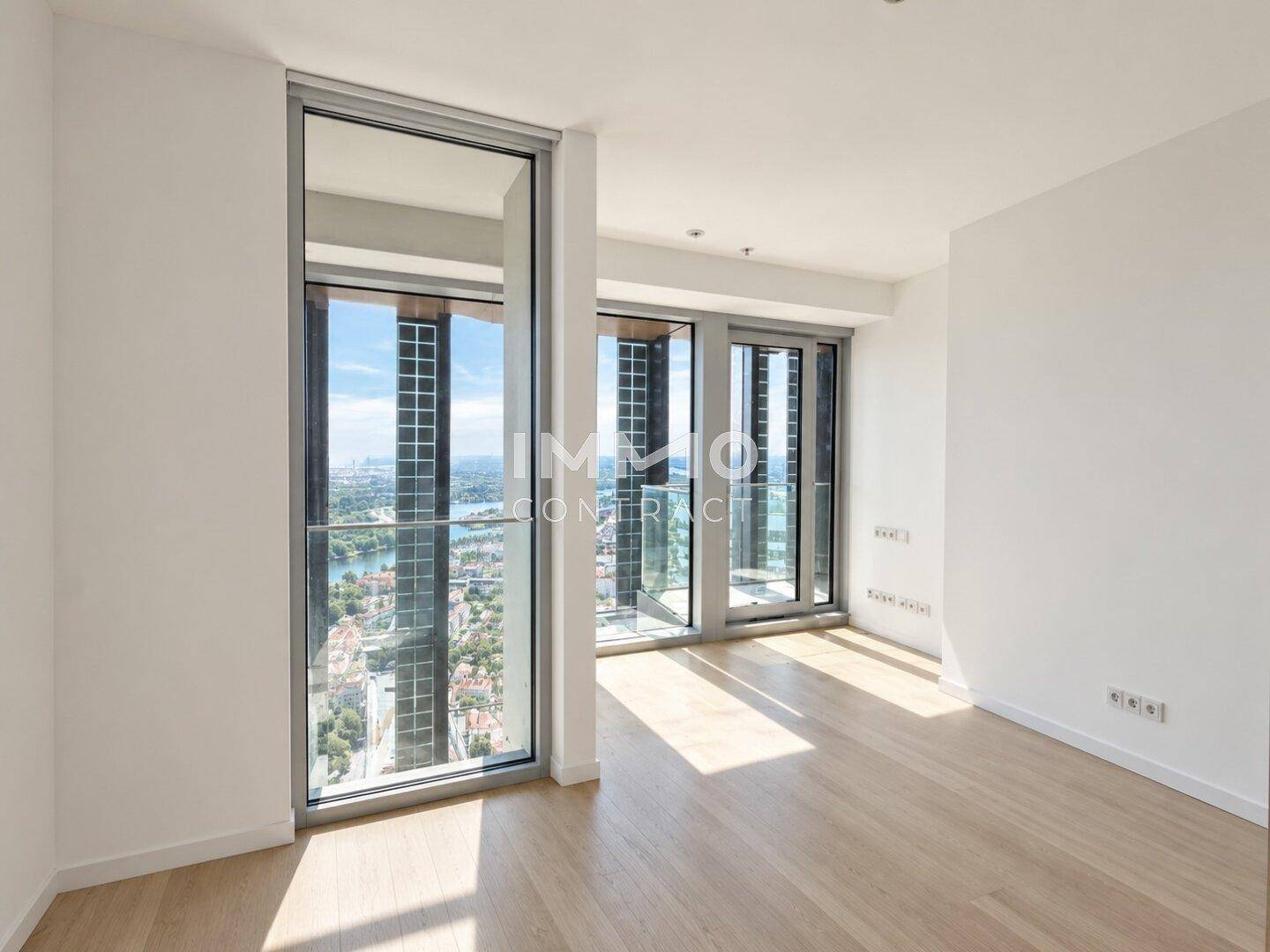 Leerer Raum mit hellem Holzboden und großen Fenstern, die einen weiten Stadtblick bieten.