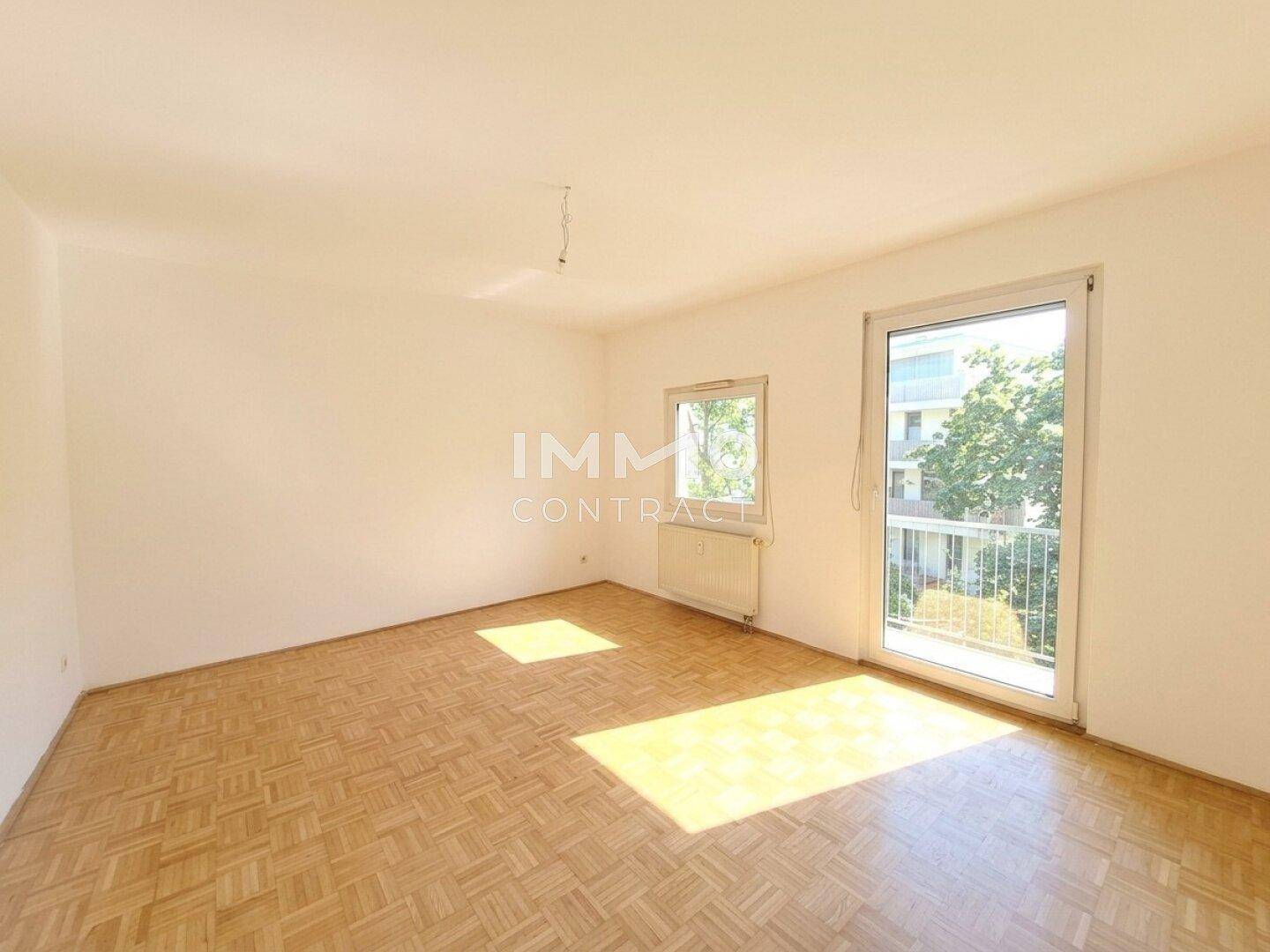 Heller, unmöblierter Raum mit Parkettboden, großen Fenstern und Zugang zum Balkon.