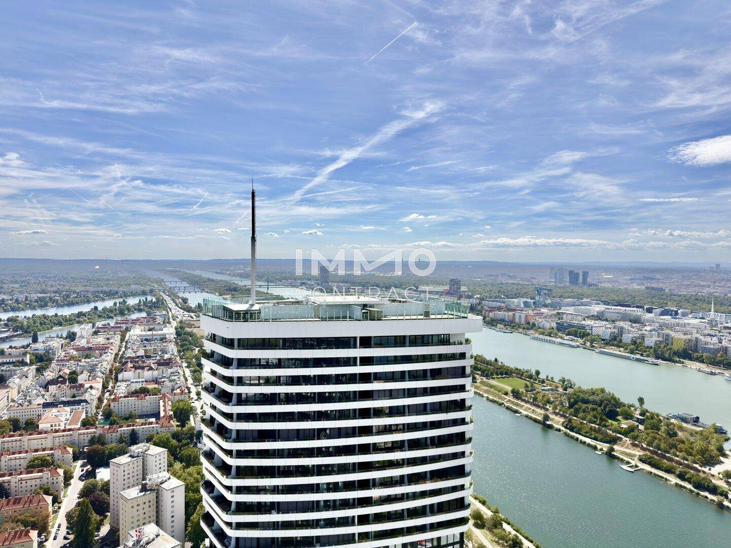 Luftaufnahme eines modernen Hochhauses mit Flachdach, umgeben von Stadt und Fluss.