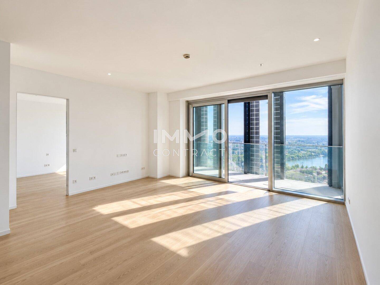 Helles, leeres Wohnzimmer mit großen Schiebetüren, Holzboden und weitem Blick auf die Stadt und den Fluss.