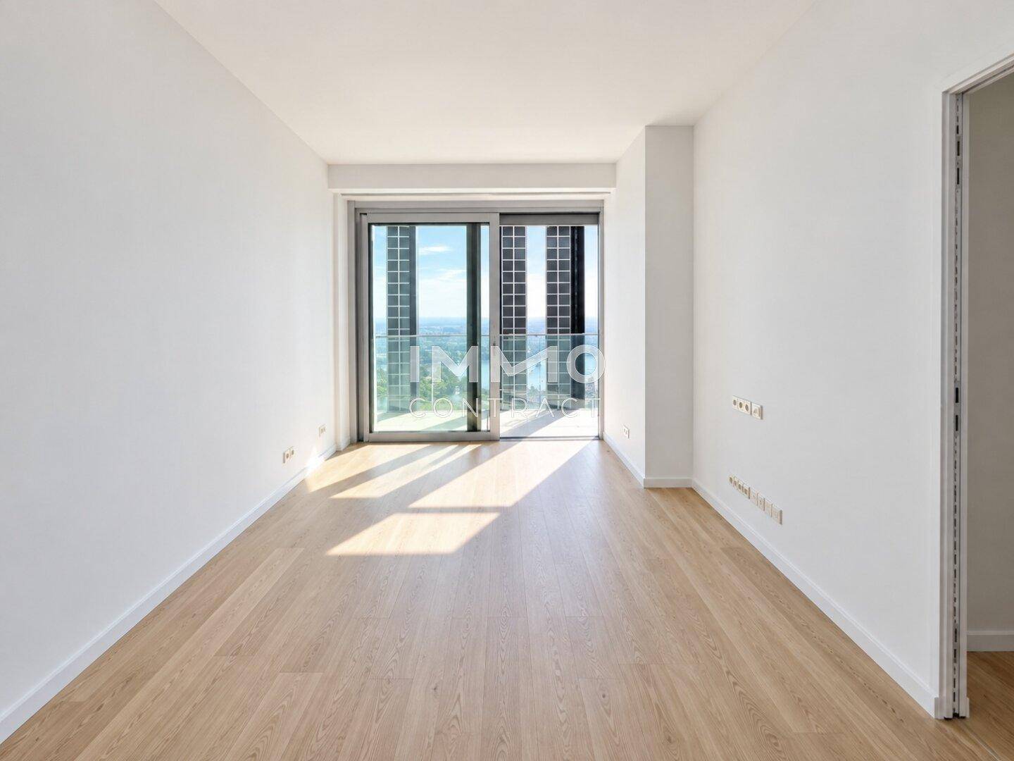 Heller Raum mit Parkettboden und Schiebetüren, die zu einem Balkon mit Aussicht führen.