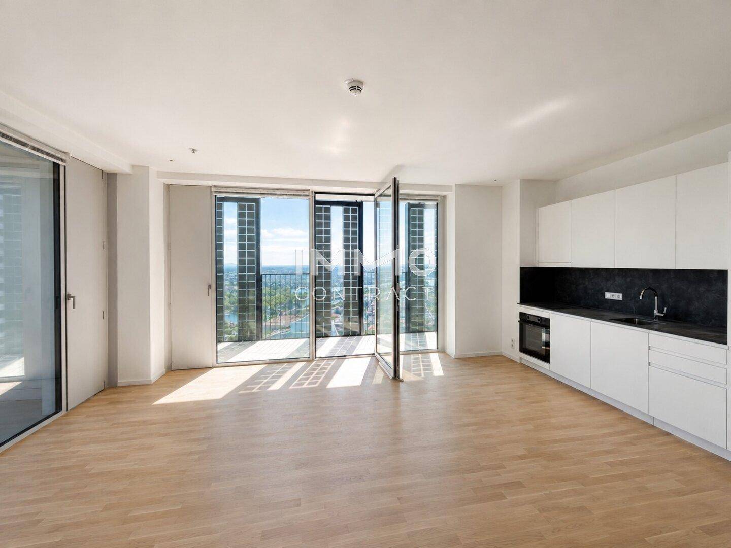 Offene Küche mit weißen Unterschränken, dunkler Arbeitsplatte und Zugang zu einem Balkon.
