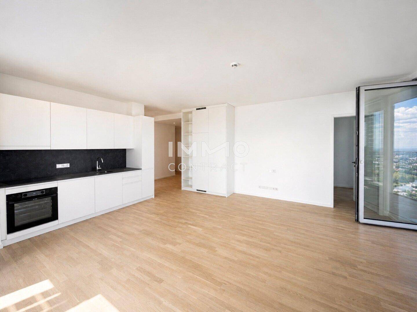 Moderne Einbauküche mit weißen Schränken, dunkler Arbeitsplatte und Holzboden in offenem Bereich.