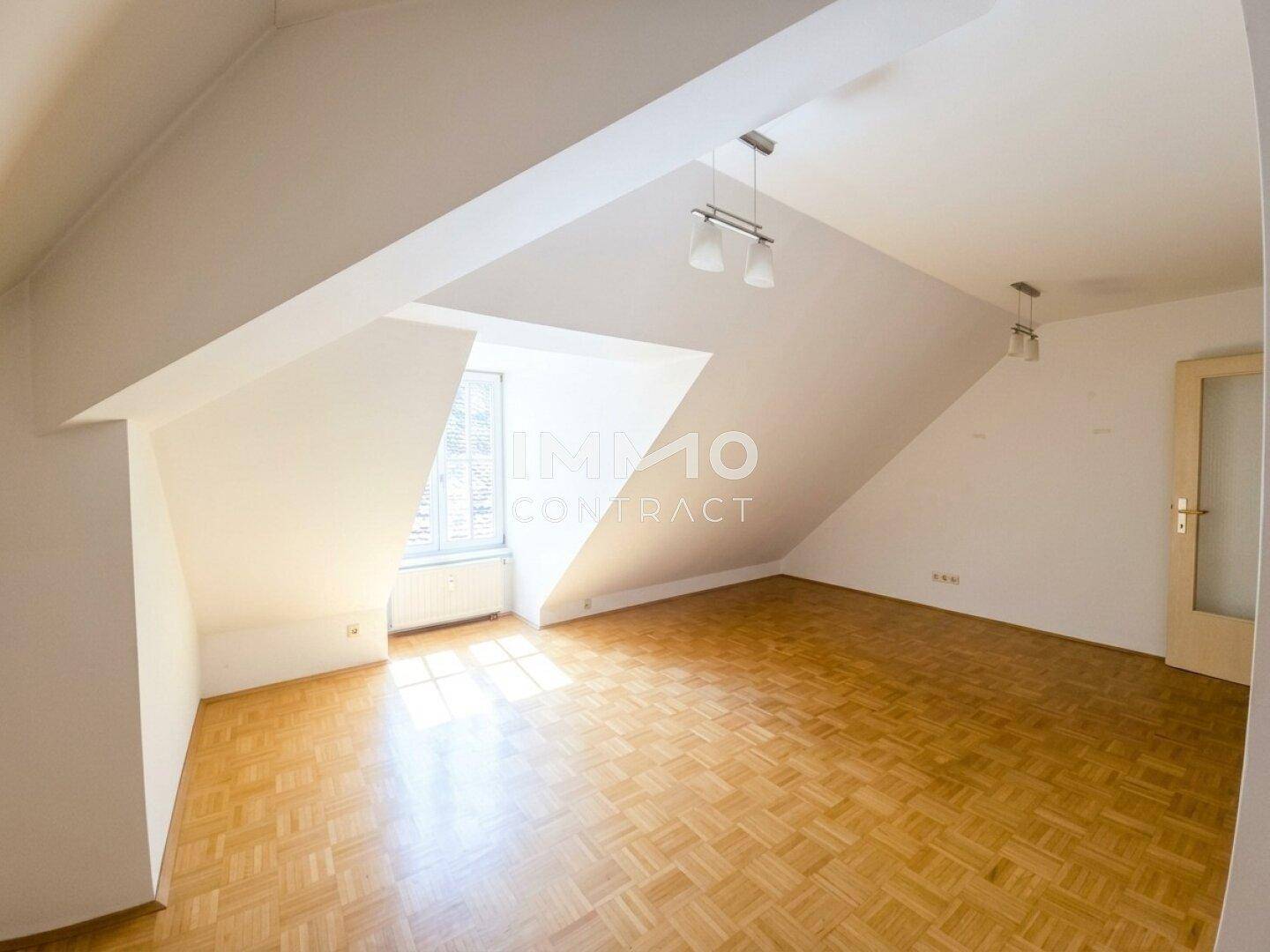 Heller Dachgeschossraum mit schrägen Wänden, Parkettboden und einem Fenster.