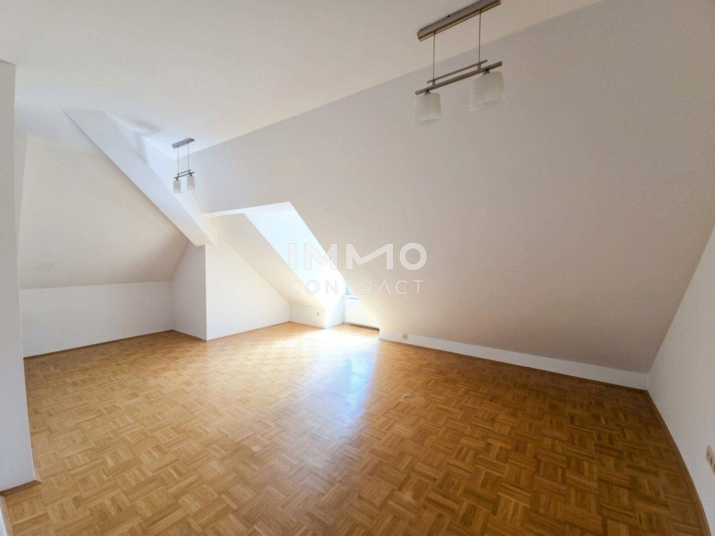 Geräumiger Dachgeschossraum mit schrägen Wänden, Parkettboden und viel natürlichem Licht.