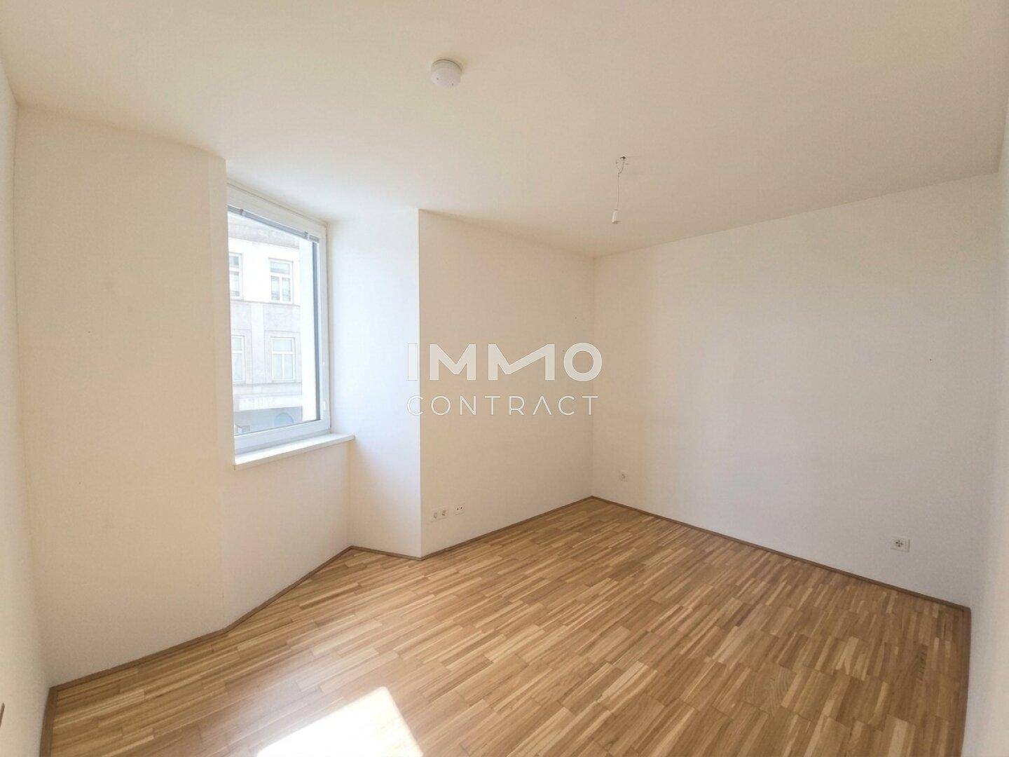 Leeres Zimmer mit hellem Parkettboden und einem Fenster, das viel Tageslicht hereinlässt.
