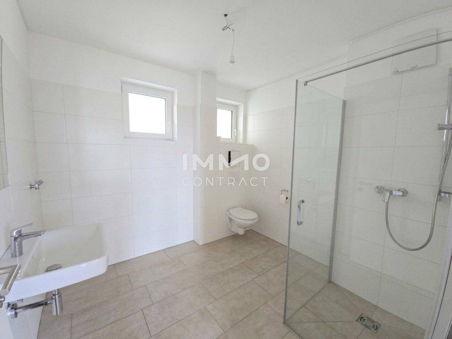 Modernes Badezimmer mit begehbarer Dusche, WC, Waschbecken und zwei Fenstern für Tageslicht.