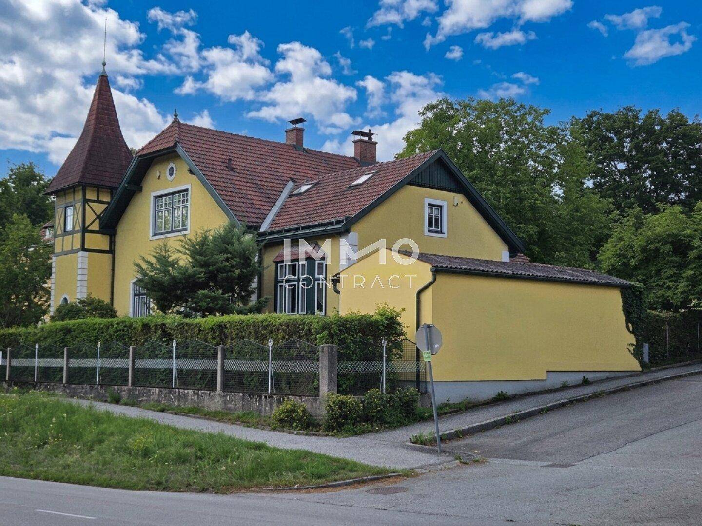 Seitenansicht des historischen gelben Hauses mit rotem Ziegeldach und üppiger Vegetation.