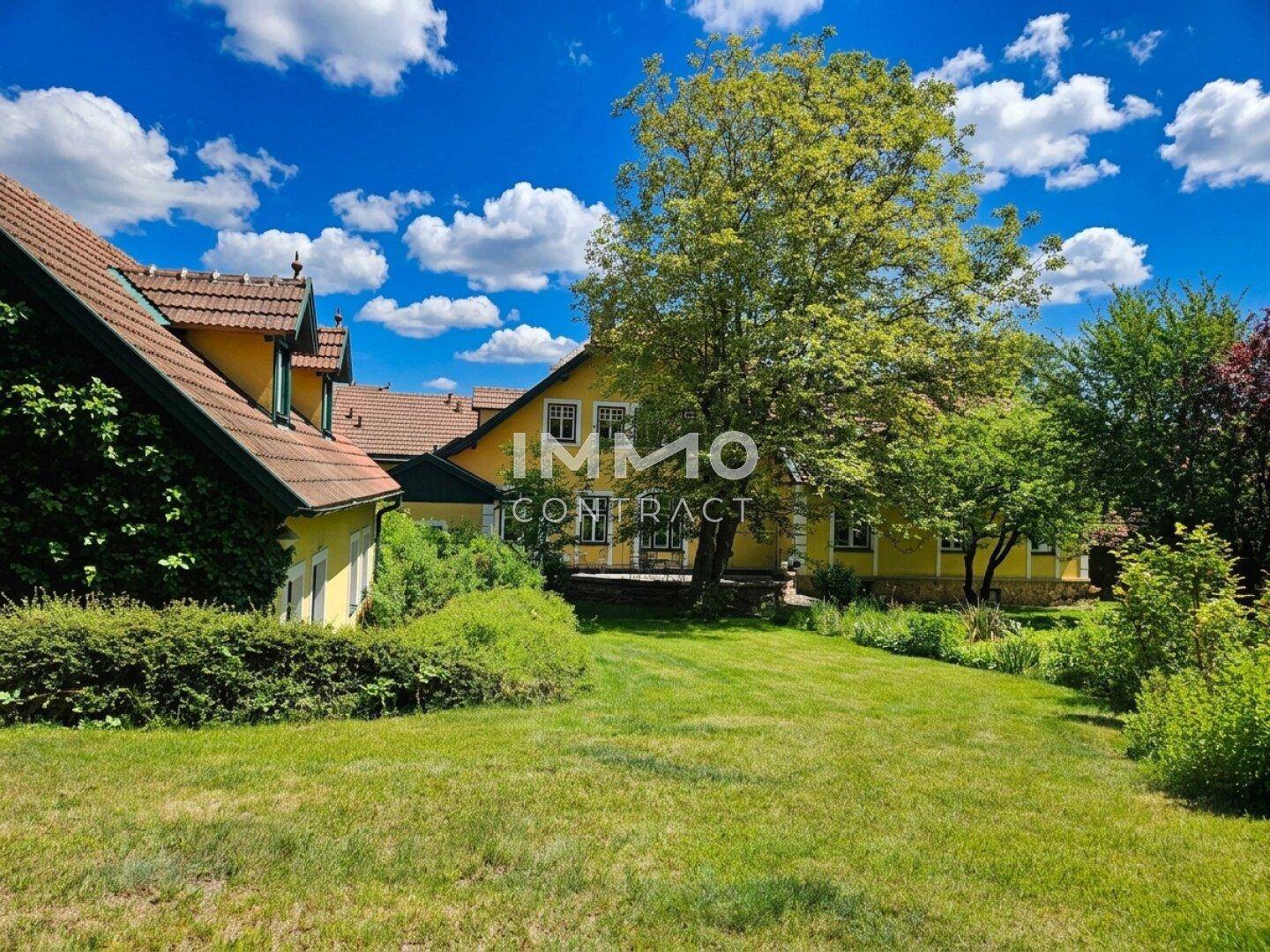 Großer, sonniger Garten mit weitläufiger Rasenfläche und altem Baumbestand hinter dem historischen Haus.
