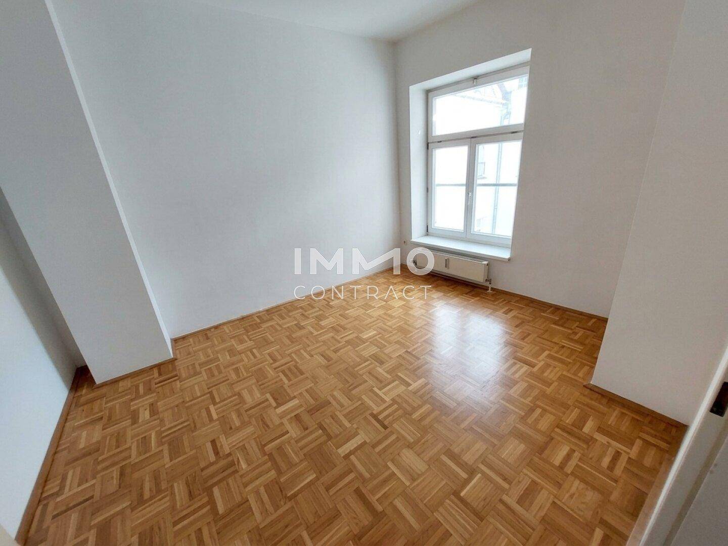 Leeres Schlafzimmer mit hellem Parkettboden und großem Fenster für natürliche Belichtung.