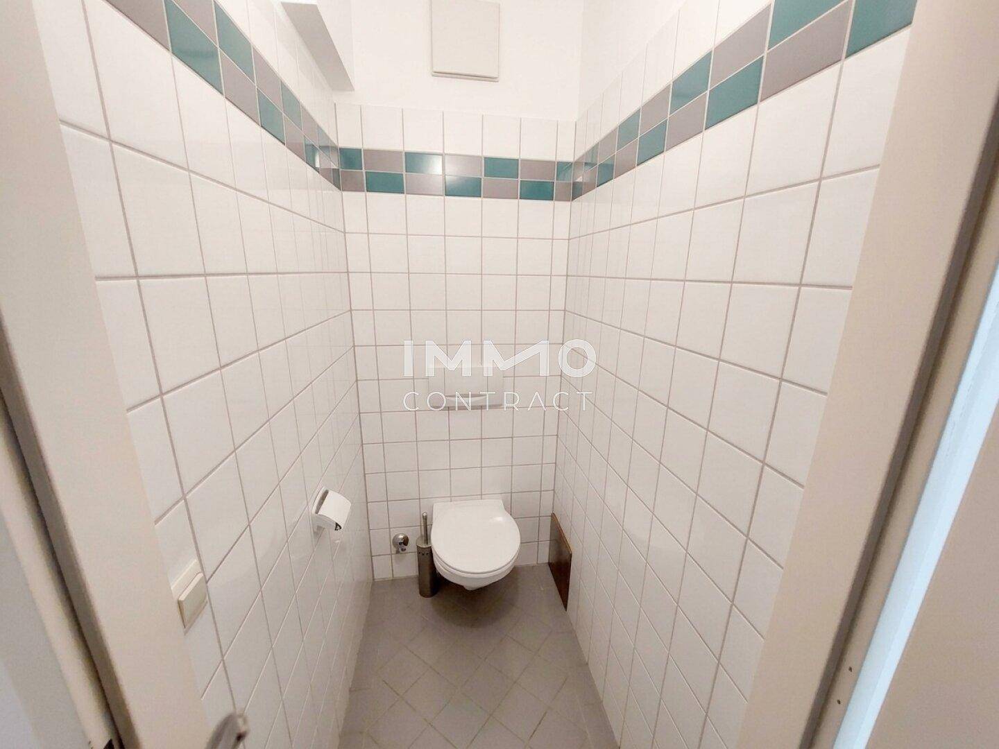 Separate Toilette mit weißen Fliesen, dekorativem Streifen und wandhängendem WC.